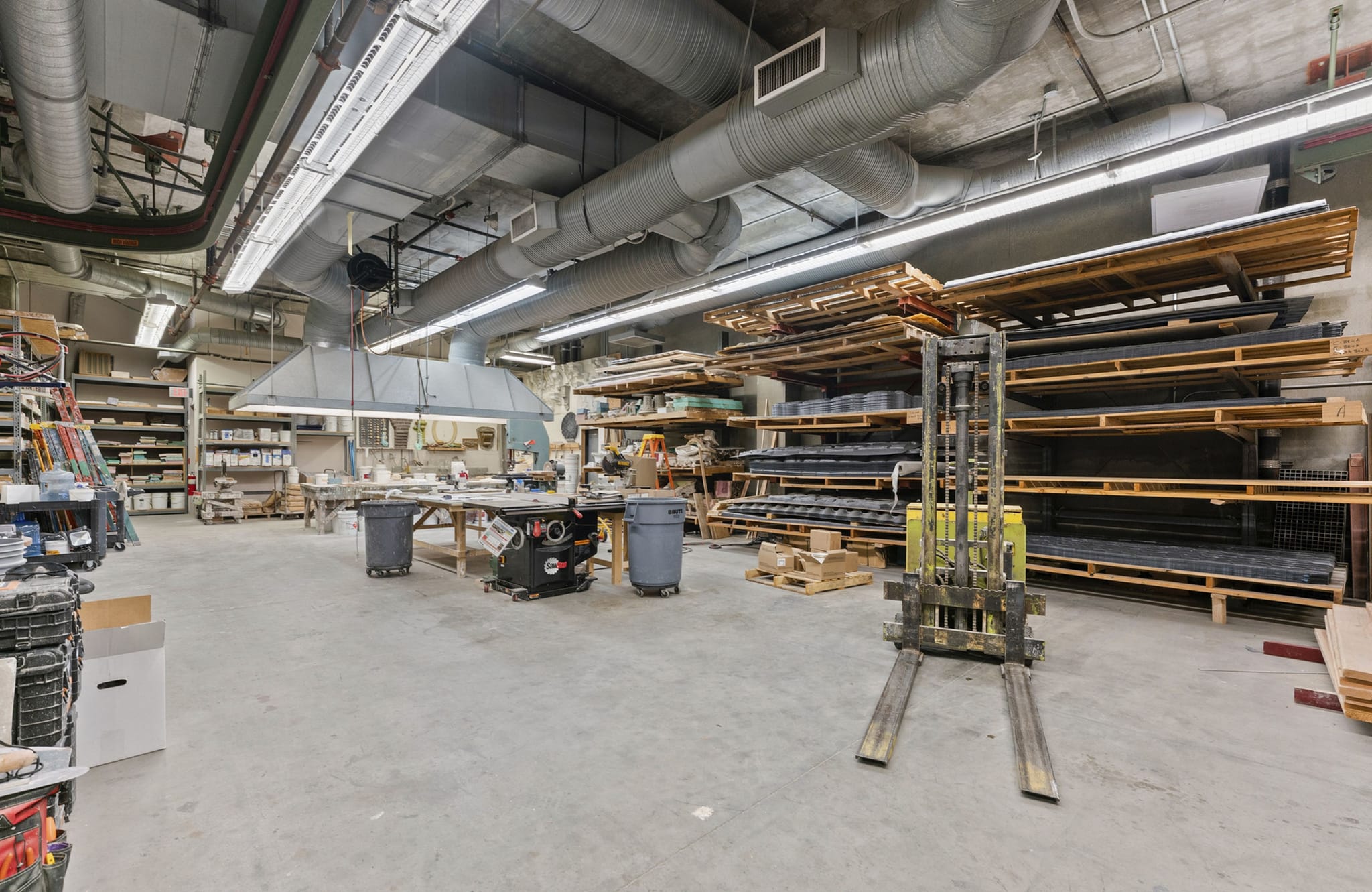 Workshop with a forklift, lumber on shelves, and woodworking tools.