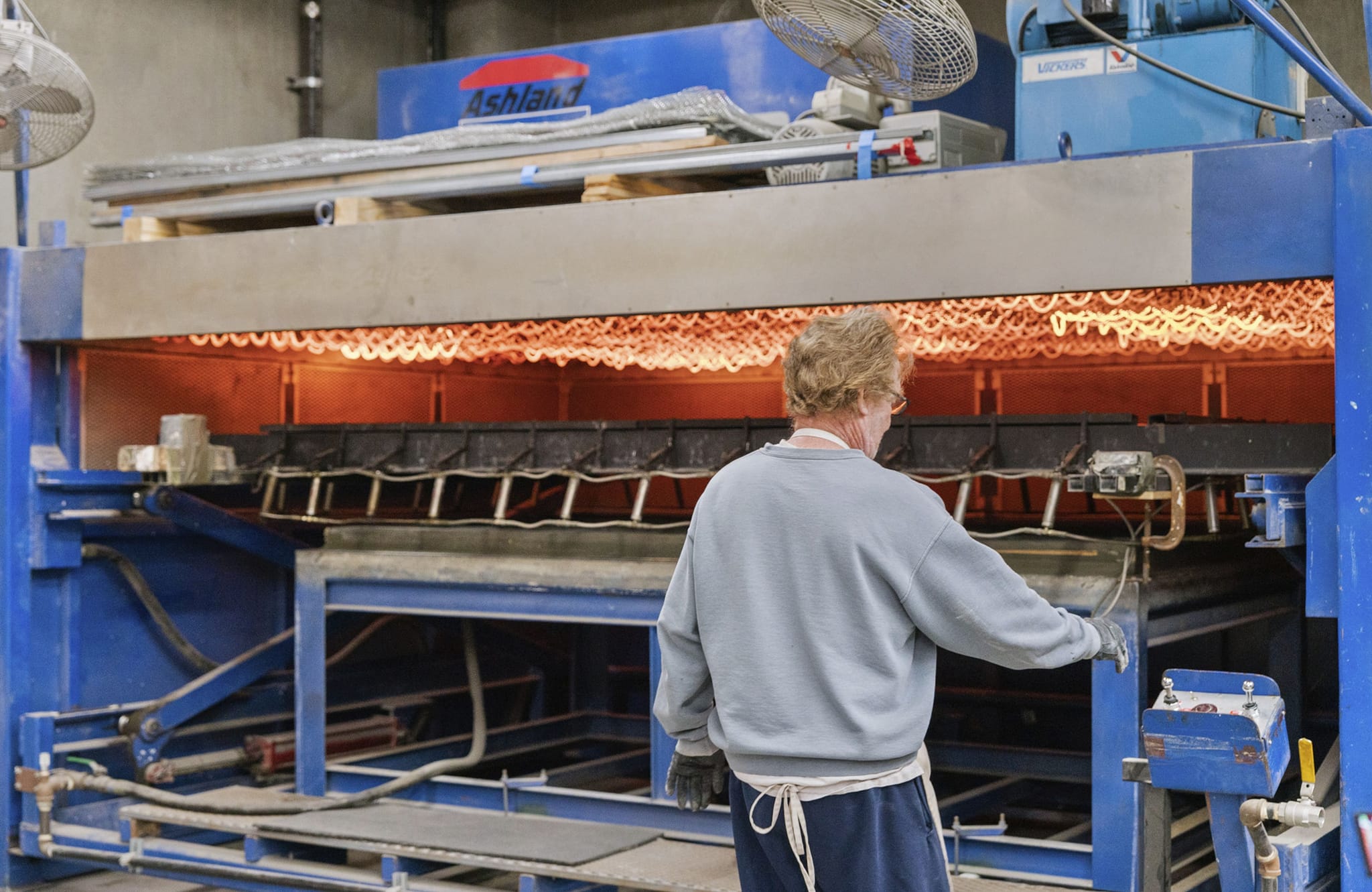A worker operates an industrial oven with glowing orange heating elements.