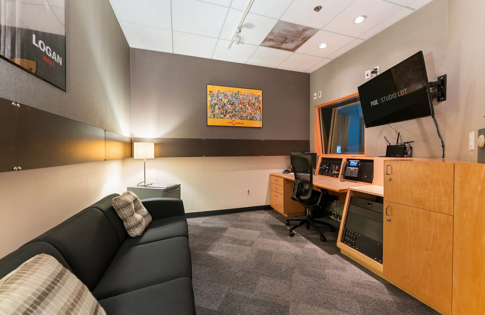 A media studio control room with a mixing desk, monitor showing "FOX STUDIO LOT", and a dark gray sofa.