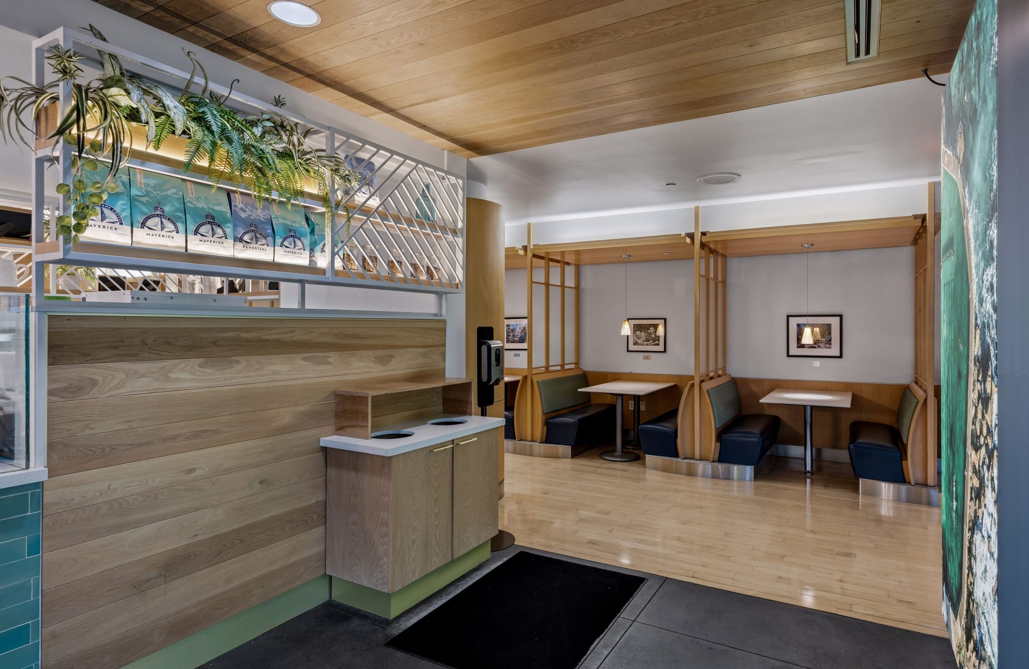Modern cafe interior with a wooden counter and ceiling, plants, and booth seating in wooden partitions.