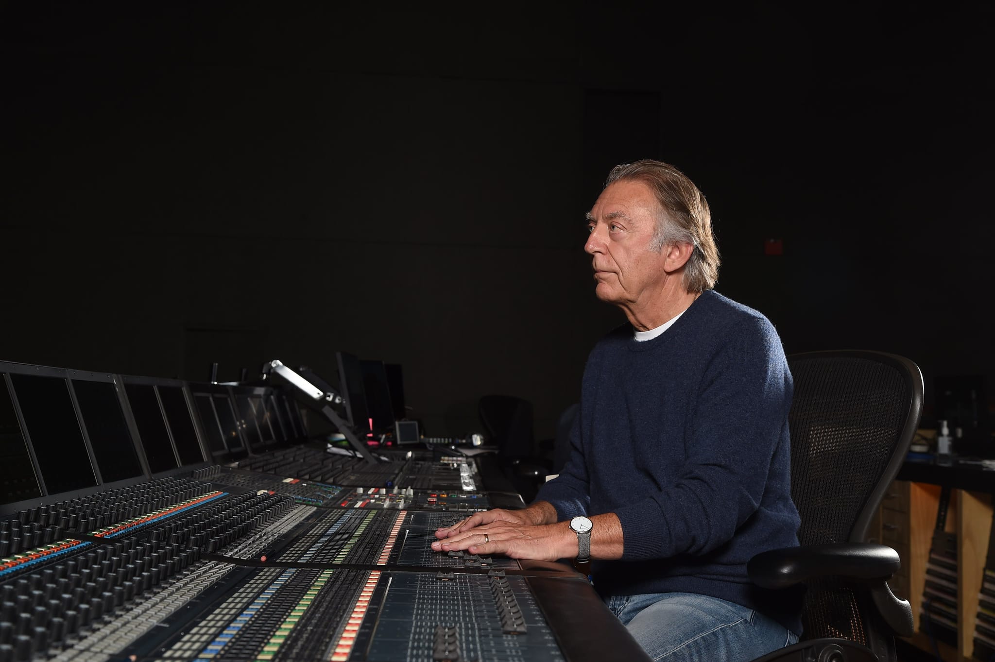 An older man in side profile sits at a large audio mixing console.