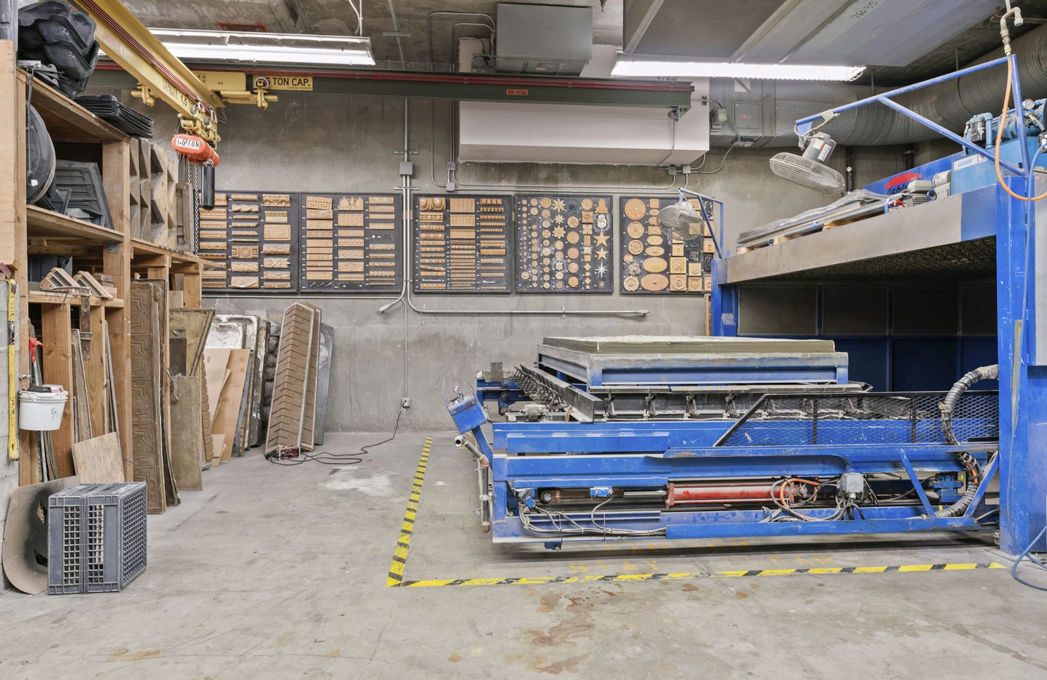 Industrial workshop with a large blue material-forming machine, shelves, and wall displays of patterns.