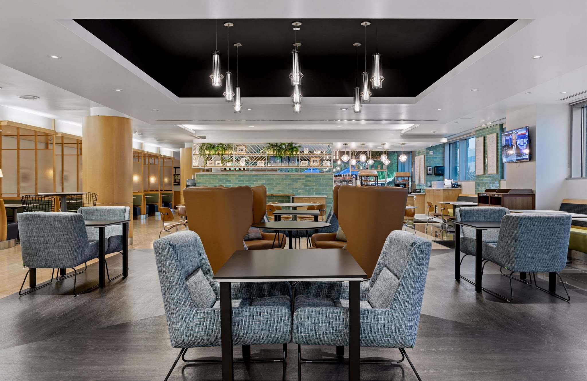 An empty, modern cafe or lounge with diverse seating, including blue armchairs and brown booths, under pendant lights.