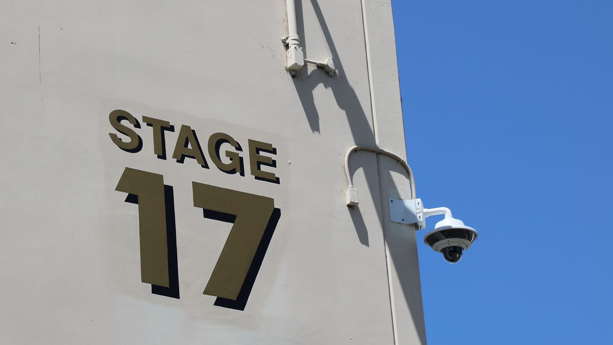 Building exterior with "STAGE 17" sign and a security camera against a blue sky.