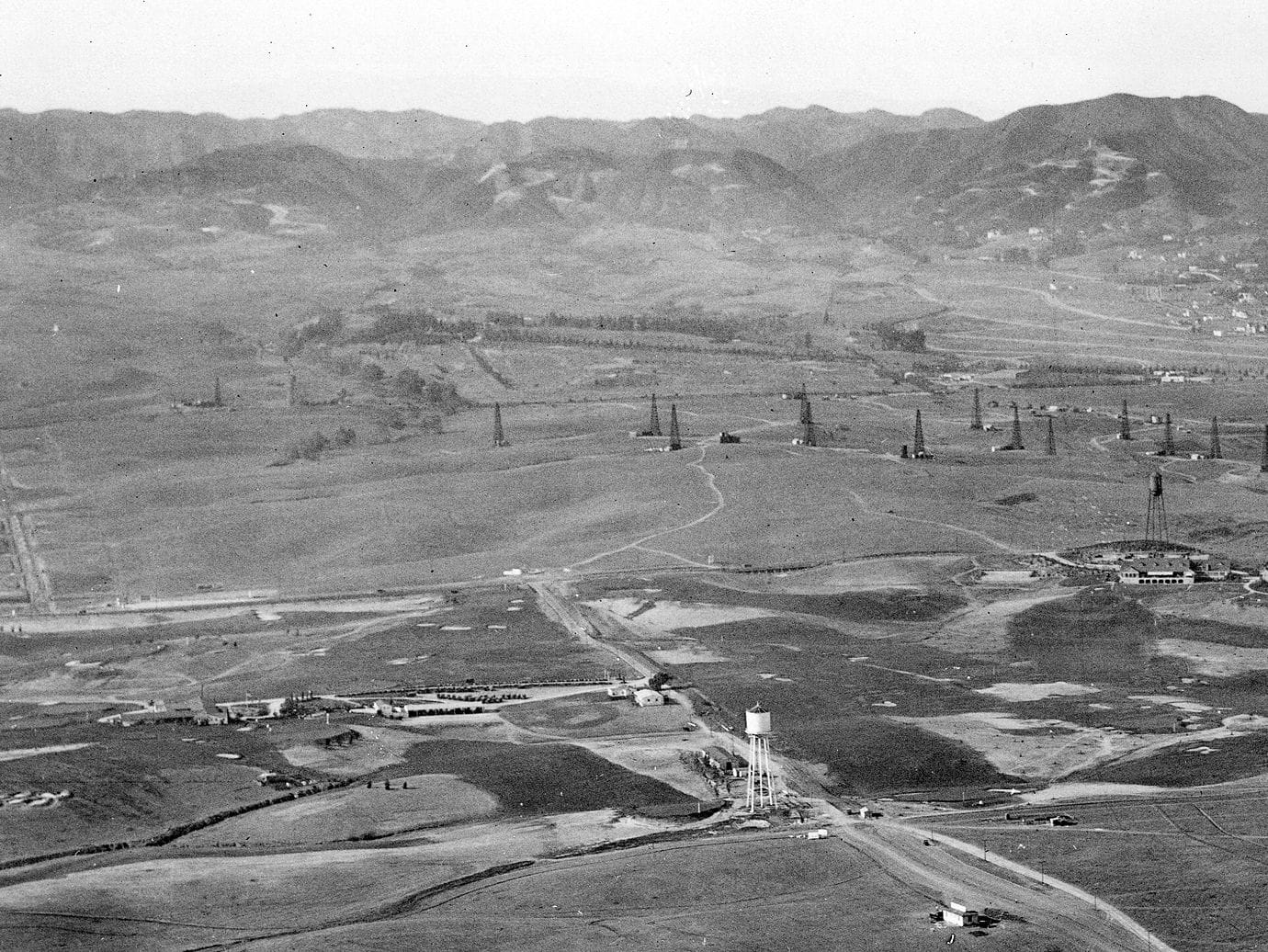 Aerial black and white view of an oil field in a valley with mountains in the distance.