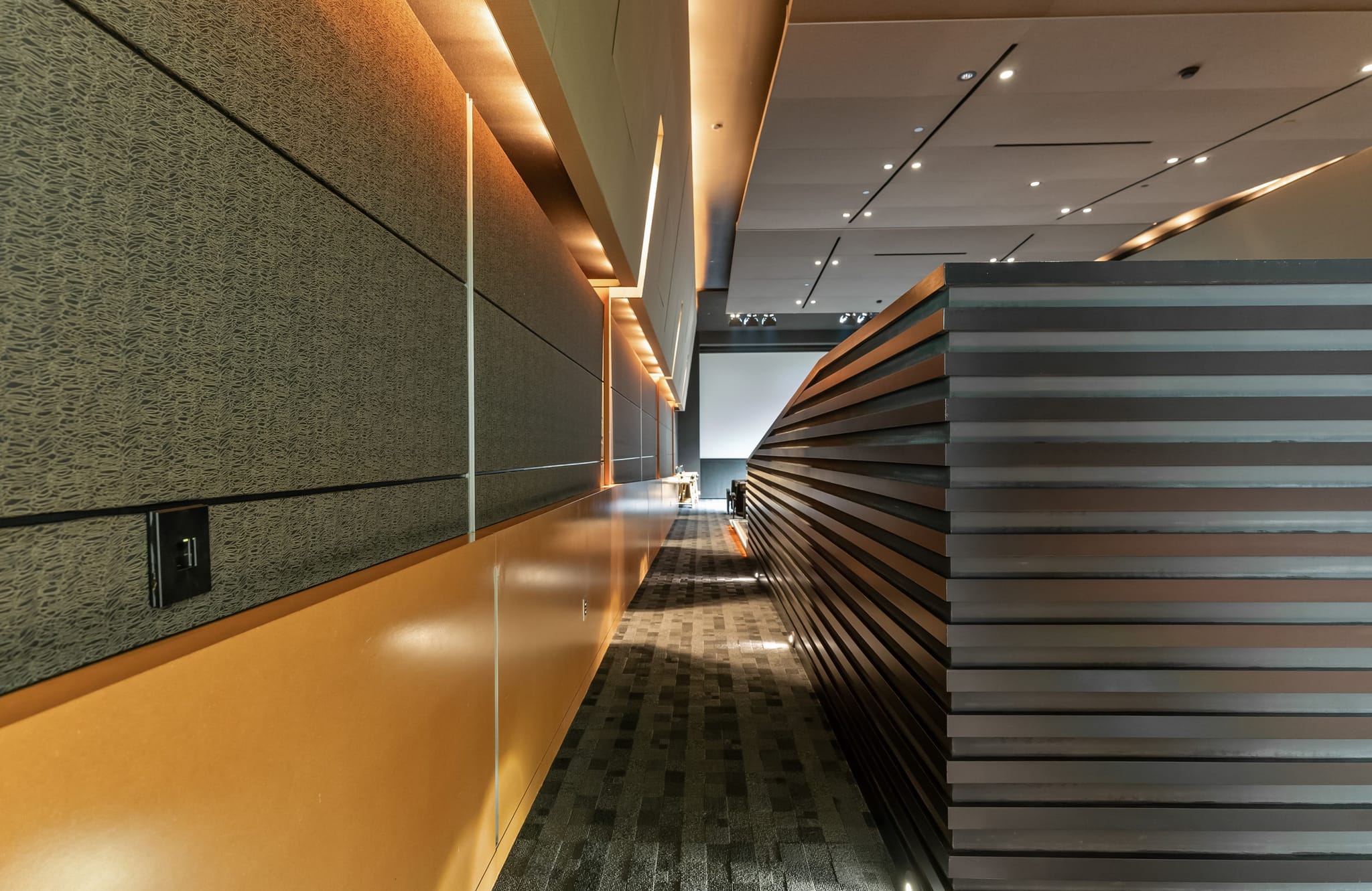 Modern interior with a textured grey wall, orange counter, and a curved, dark slatted structure under warm lighting.