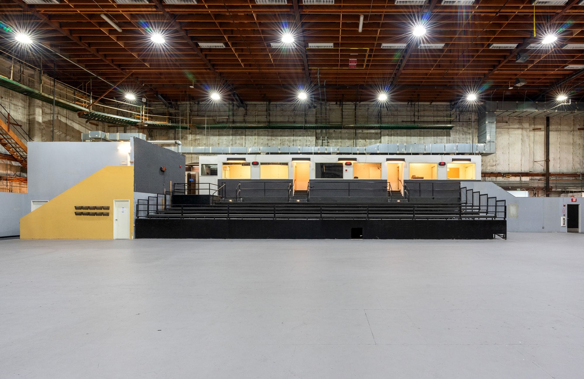 A large industrial space with a high wooden beam ceiling, bright lights, and a central elevated structure containing rooms above dark tiered seating.