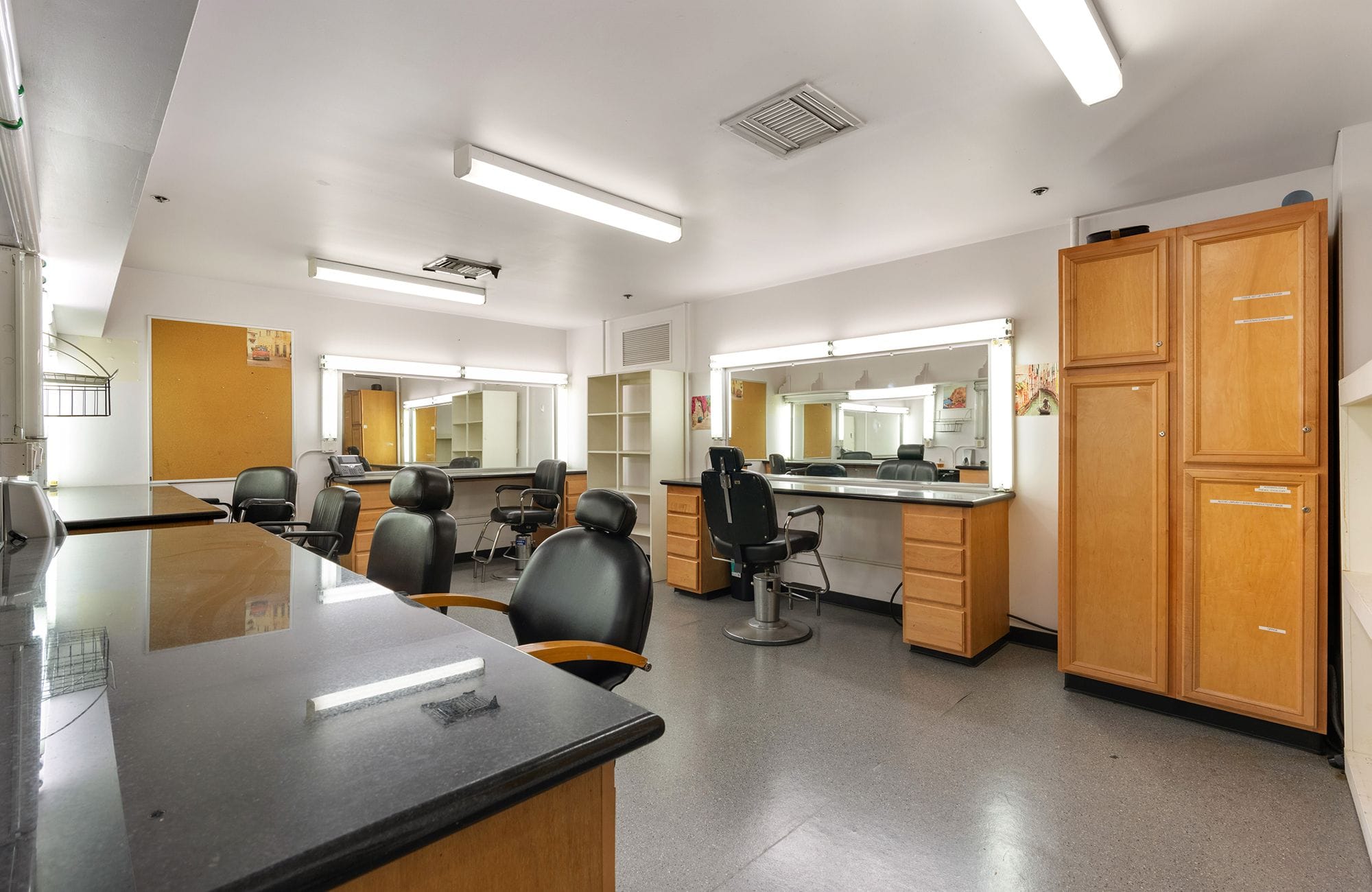 An empty dressing room with multiple lighted vanity stations and salon chairs.
