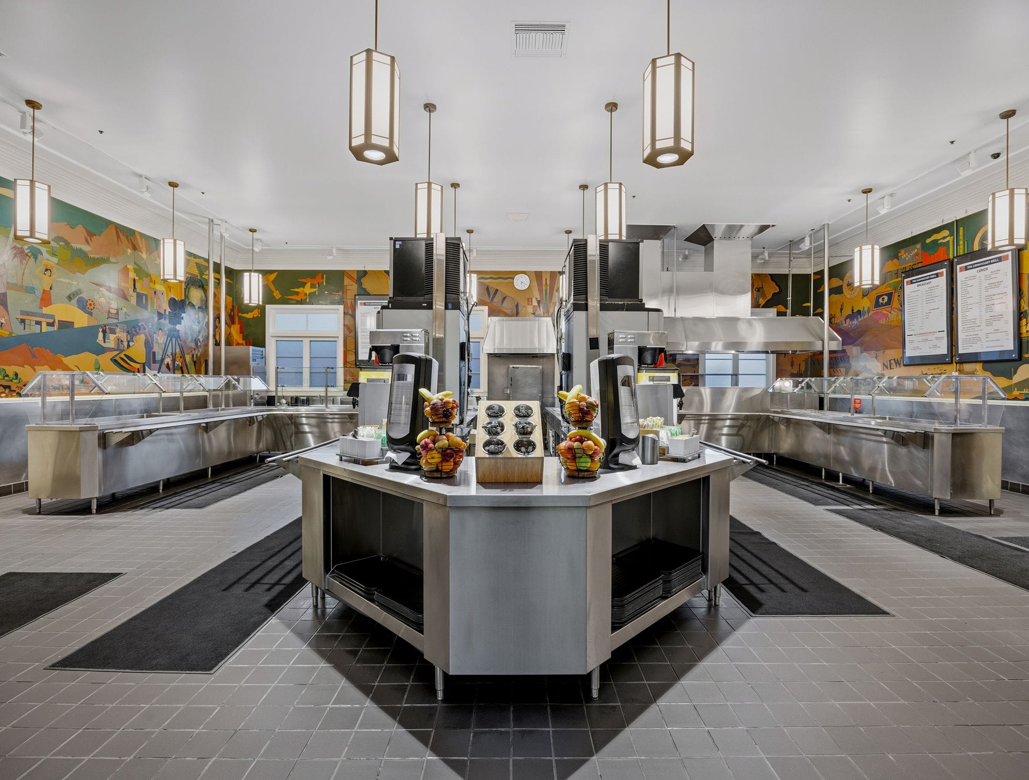 Empty cafeteria serving area with stainless steel equipment and wall murals.