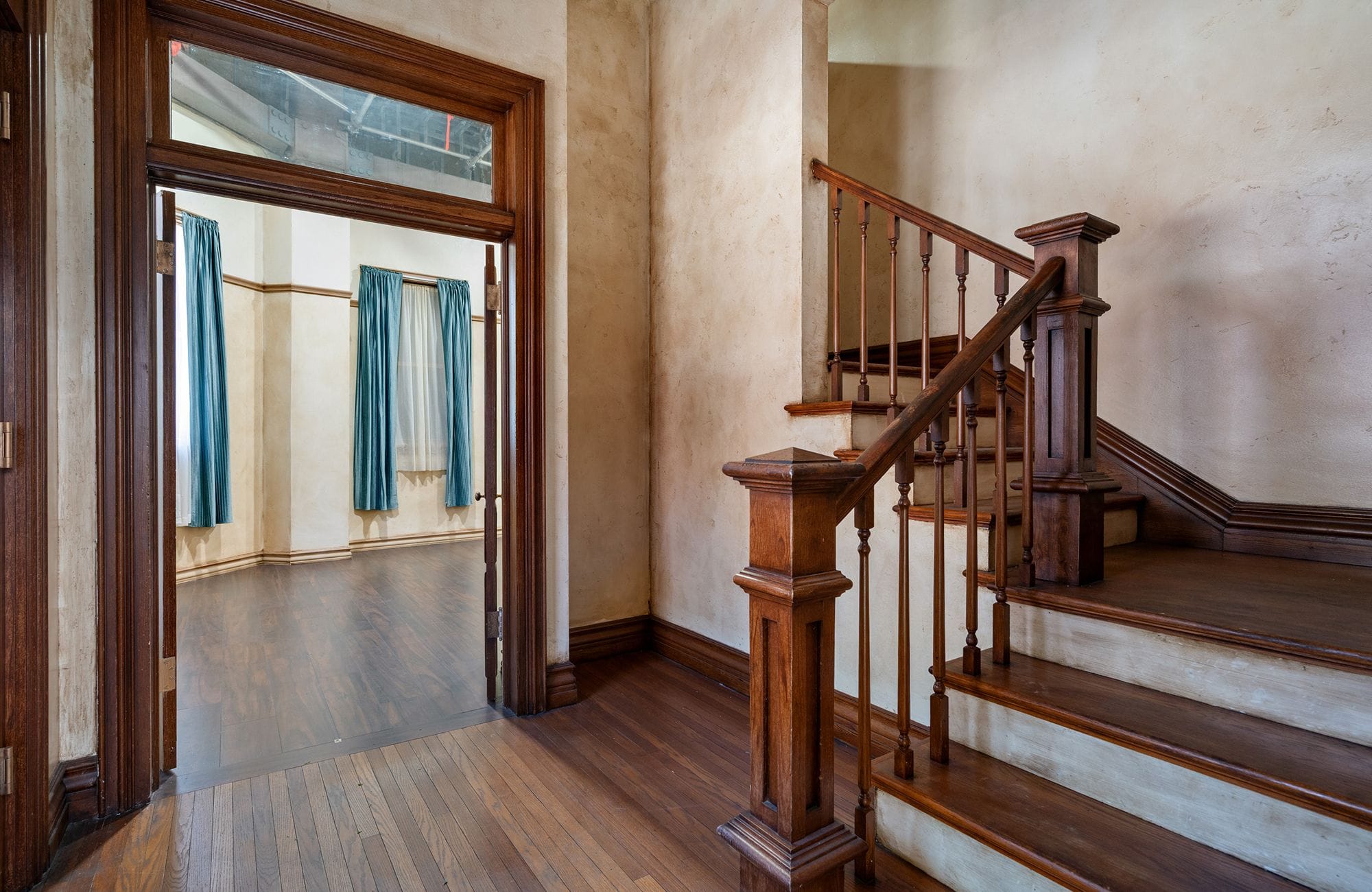 Dark wood staircase next to an open doorway revealing a room with blue curtains.