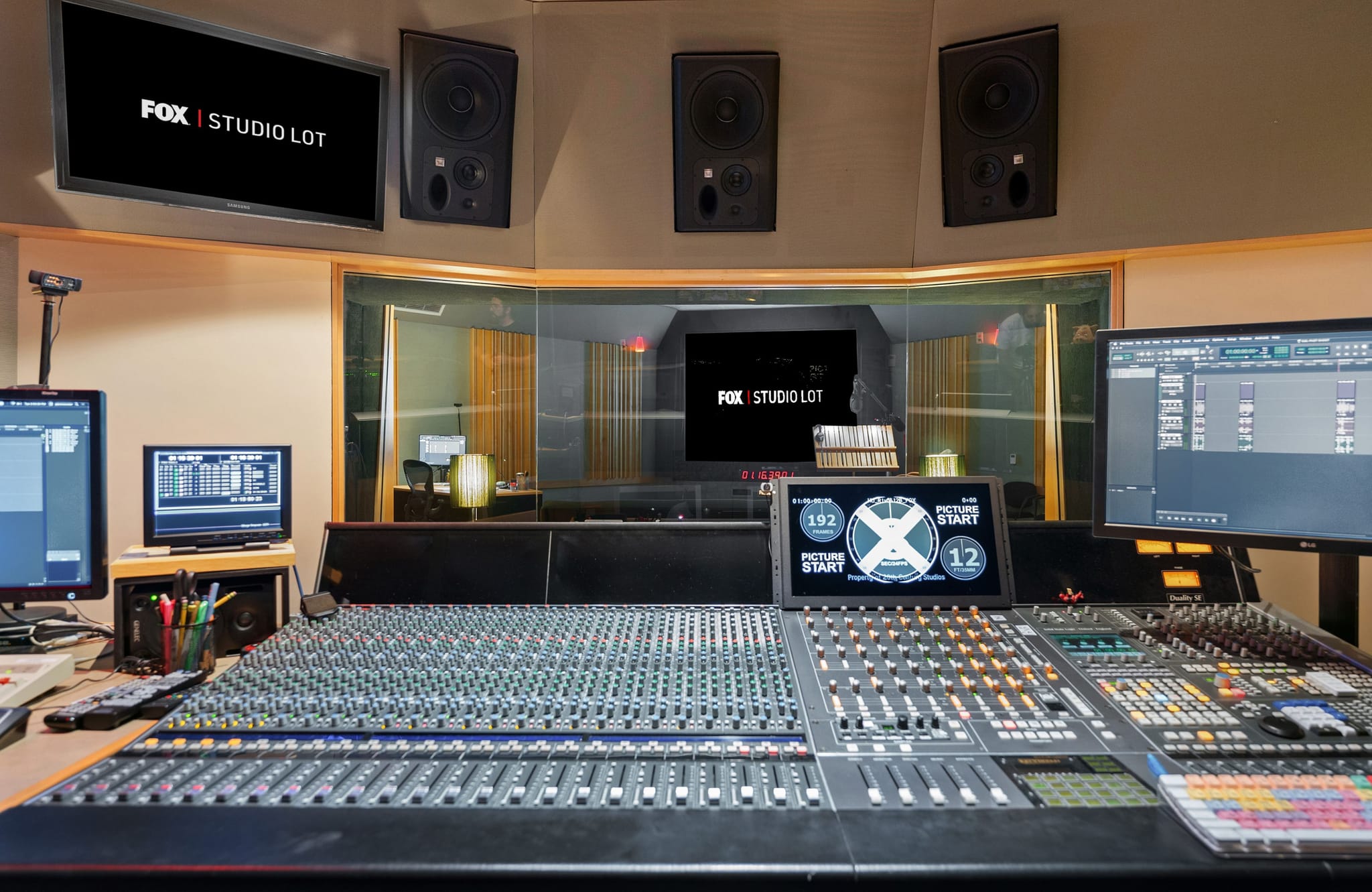 A professional recording studio control room with a large mixing console, studio monitors, and screens displaying "FOX | STUDIO LOT."