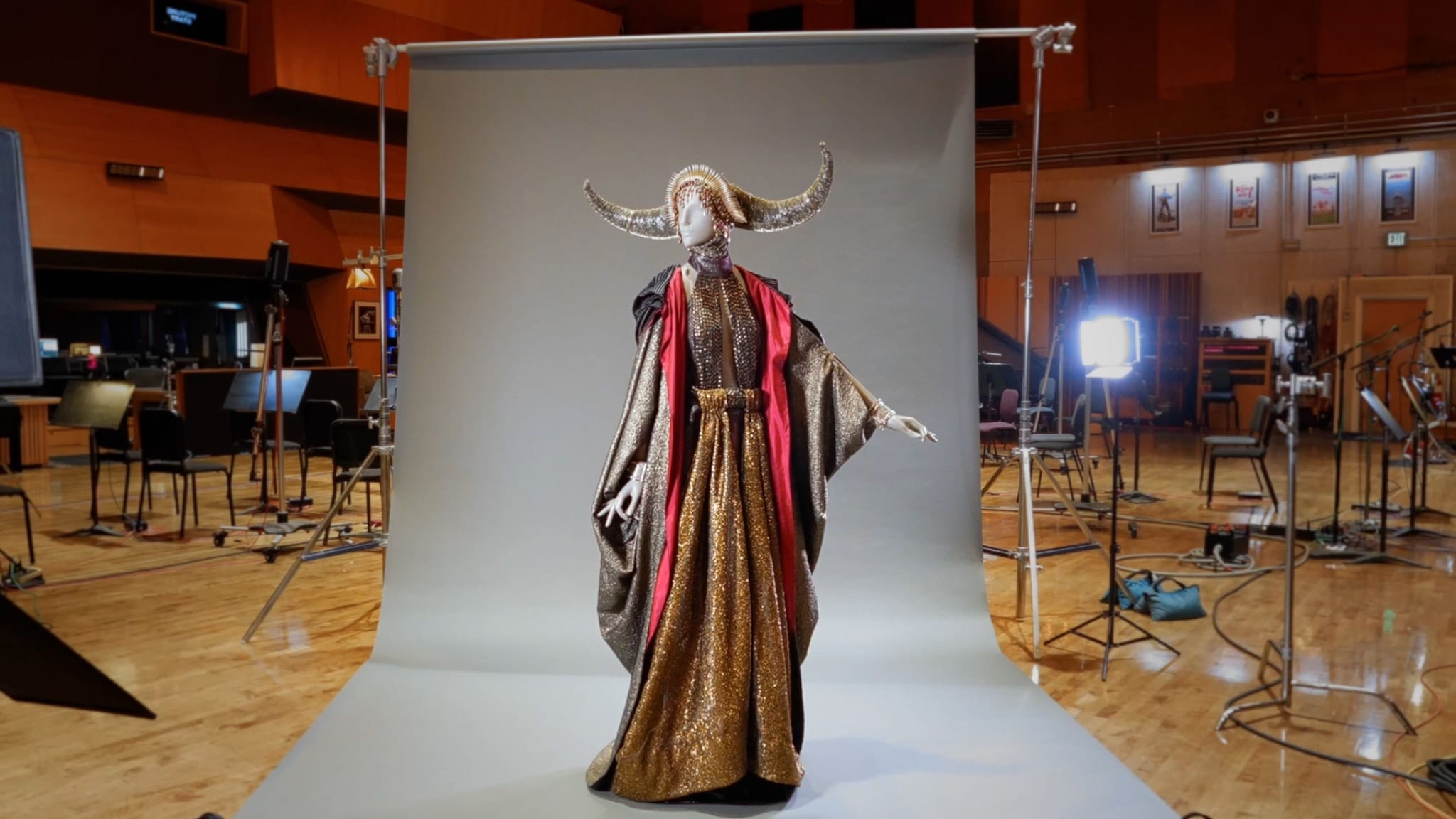 A mannequin in an elaborate golden and red costume with a horned headpiece on a grey studio backdrop.