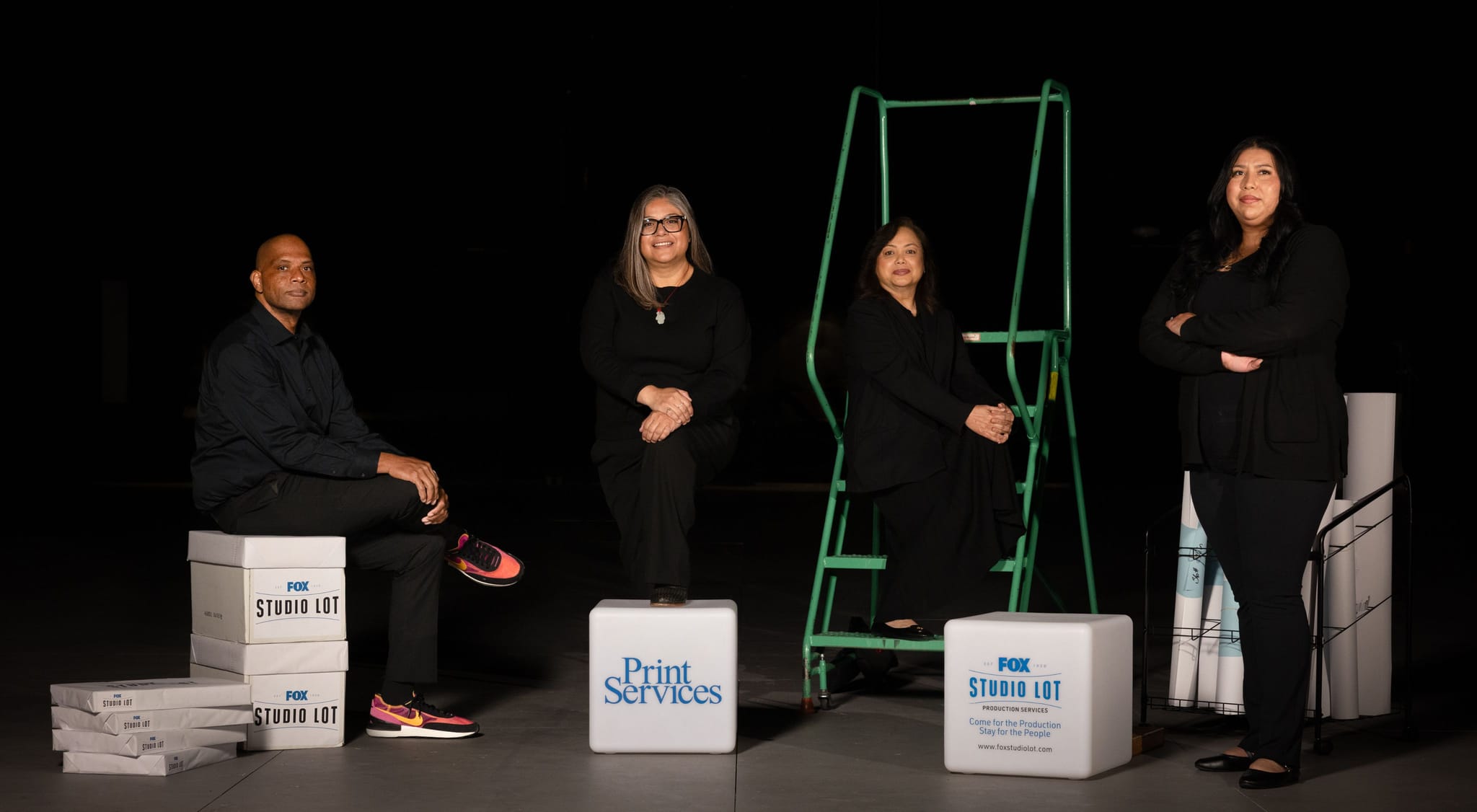 Four people in black clothing pose with print services branding and materials against a dark background.