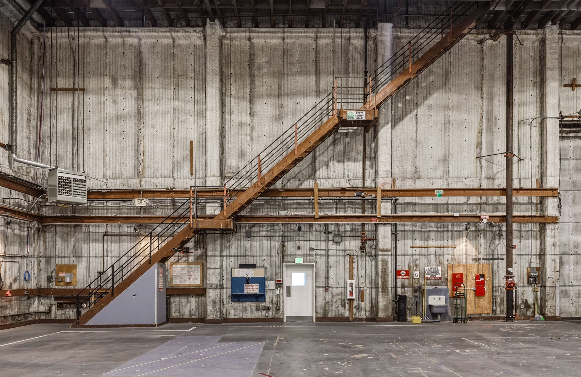 A large, industrial room with tall concrete walls and a prominent wooden staircase.