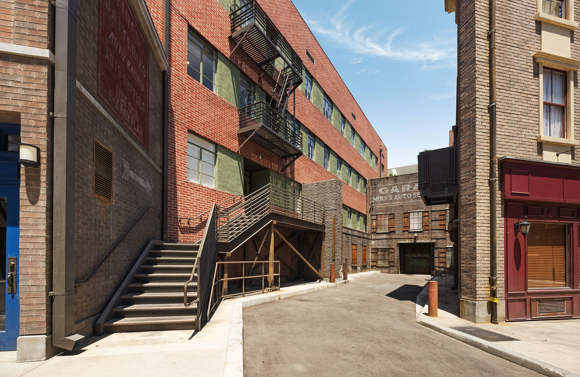 An urban alleyway with brick buildings, an external staircase, a fire escape, and a distant garage sign.