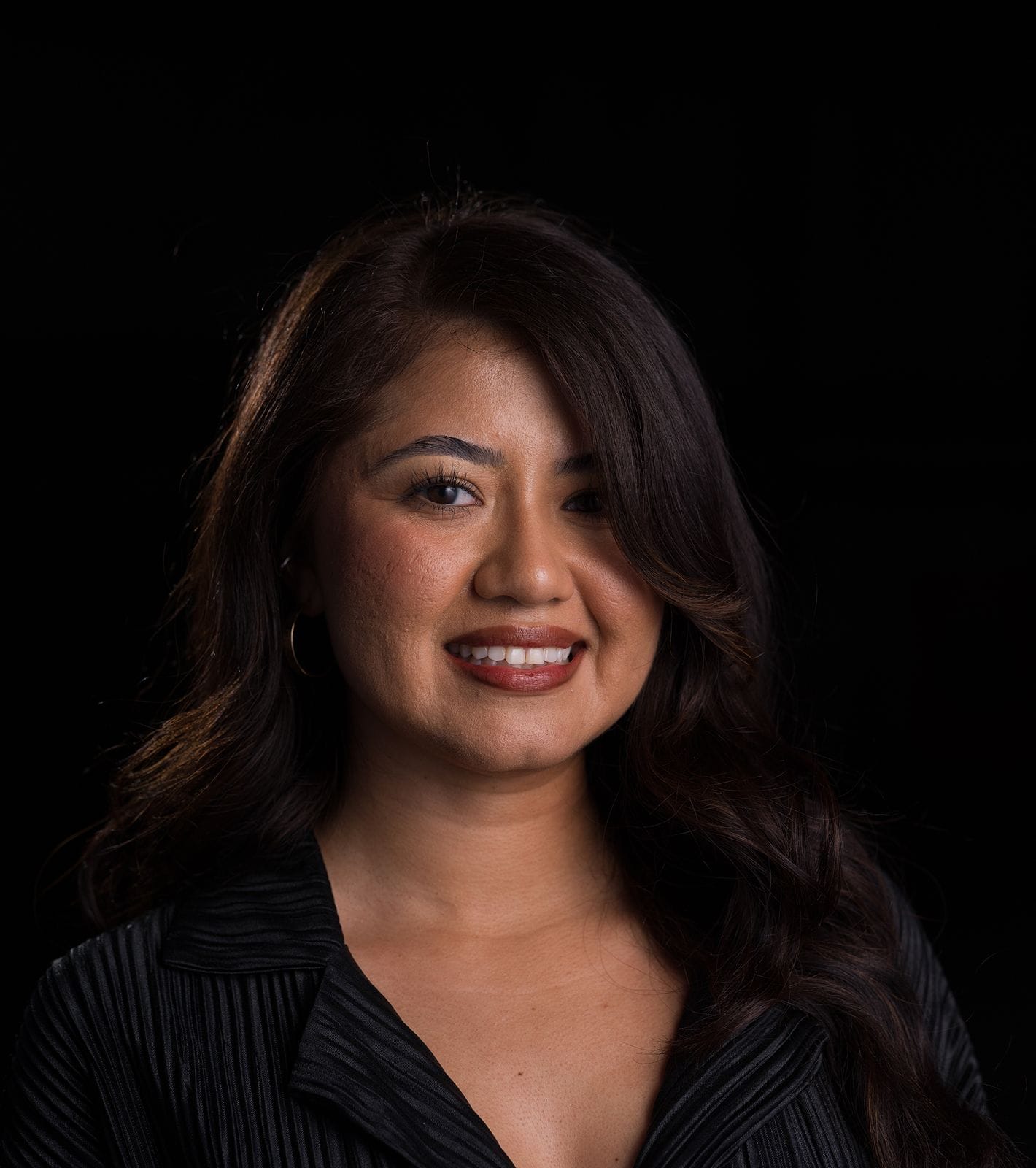 Headshot of a smiling woman with long dark hair against a black background.