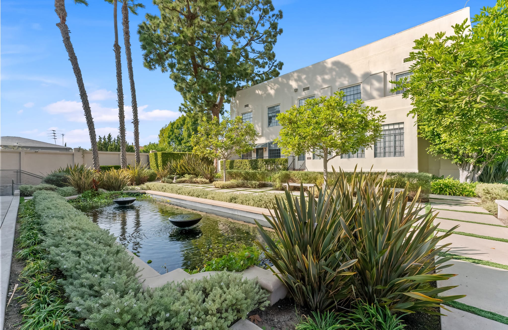 A landscaped courtyard featuring a narrow pond with two bowl fountains, set against a modern building.