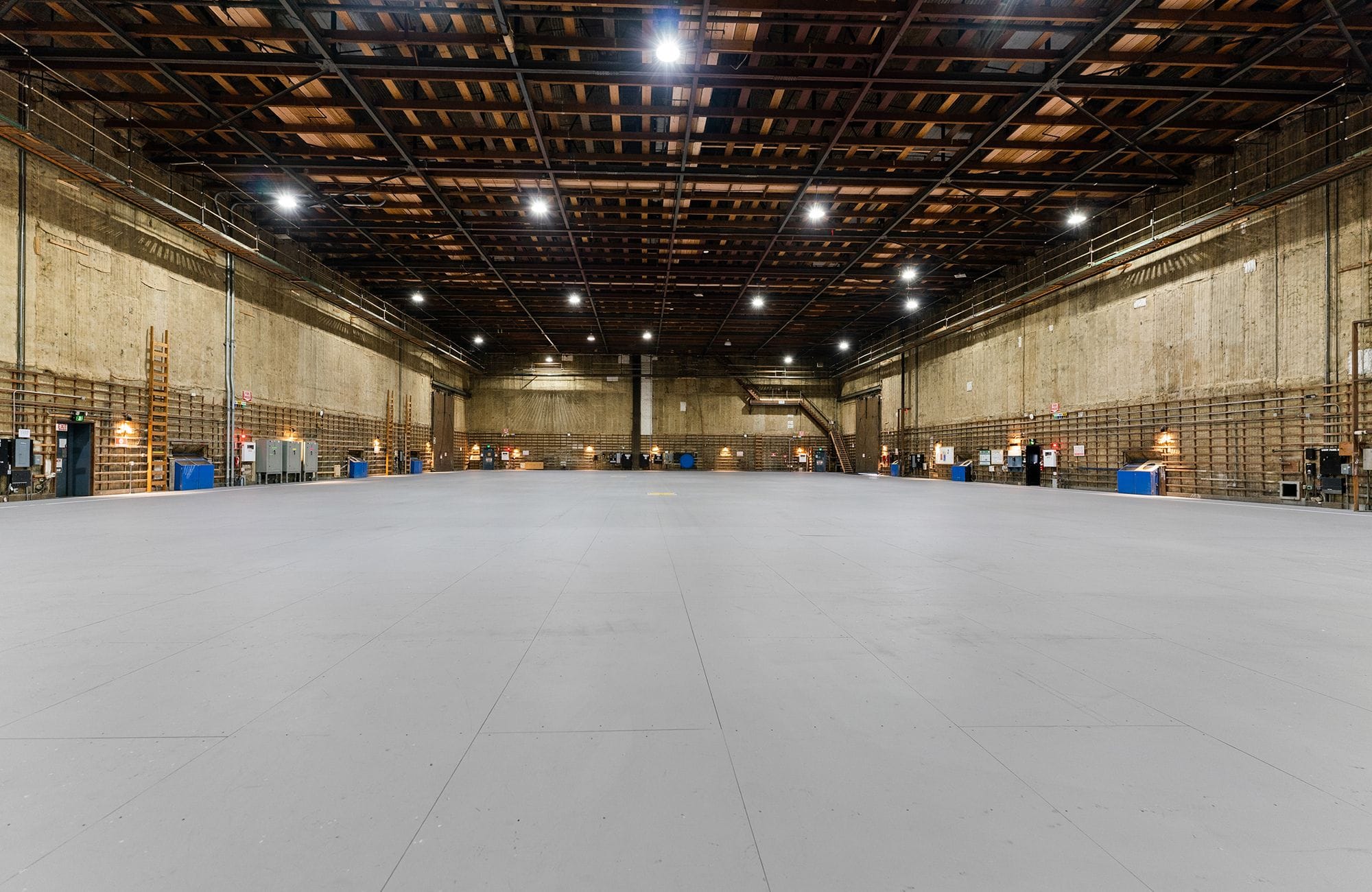 A vast, empty warehouse or production studio with high exposed beam ceilings and bright overhead lights.