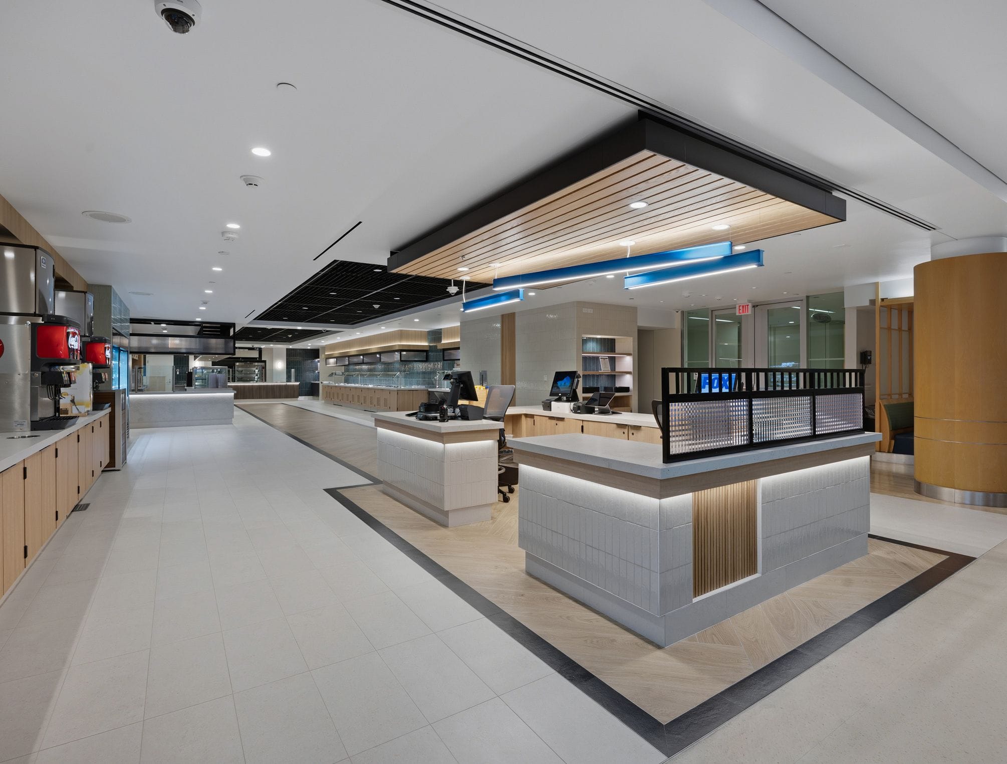 A modern, well-lit cafeteria with long serving stations, beverage dispensers, and checkout counters.