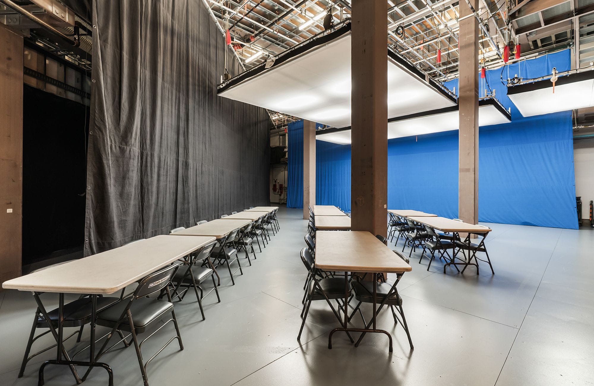 Rows of tables and chairs set up in a studio with a gray curtain on the left and a blue screen on the right.