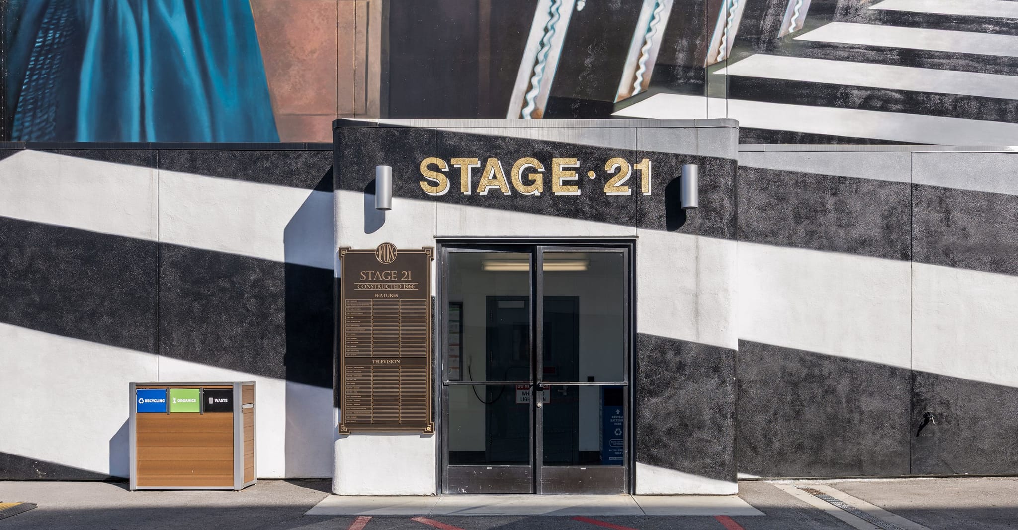 Stage 21 entrance with black and white striped walls, a bronze plaque, and a recycling station.