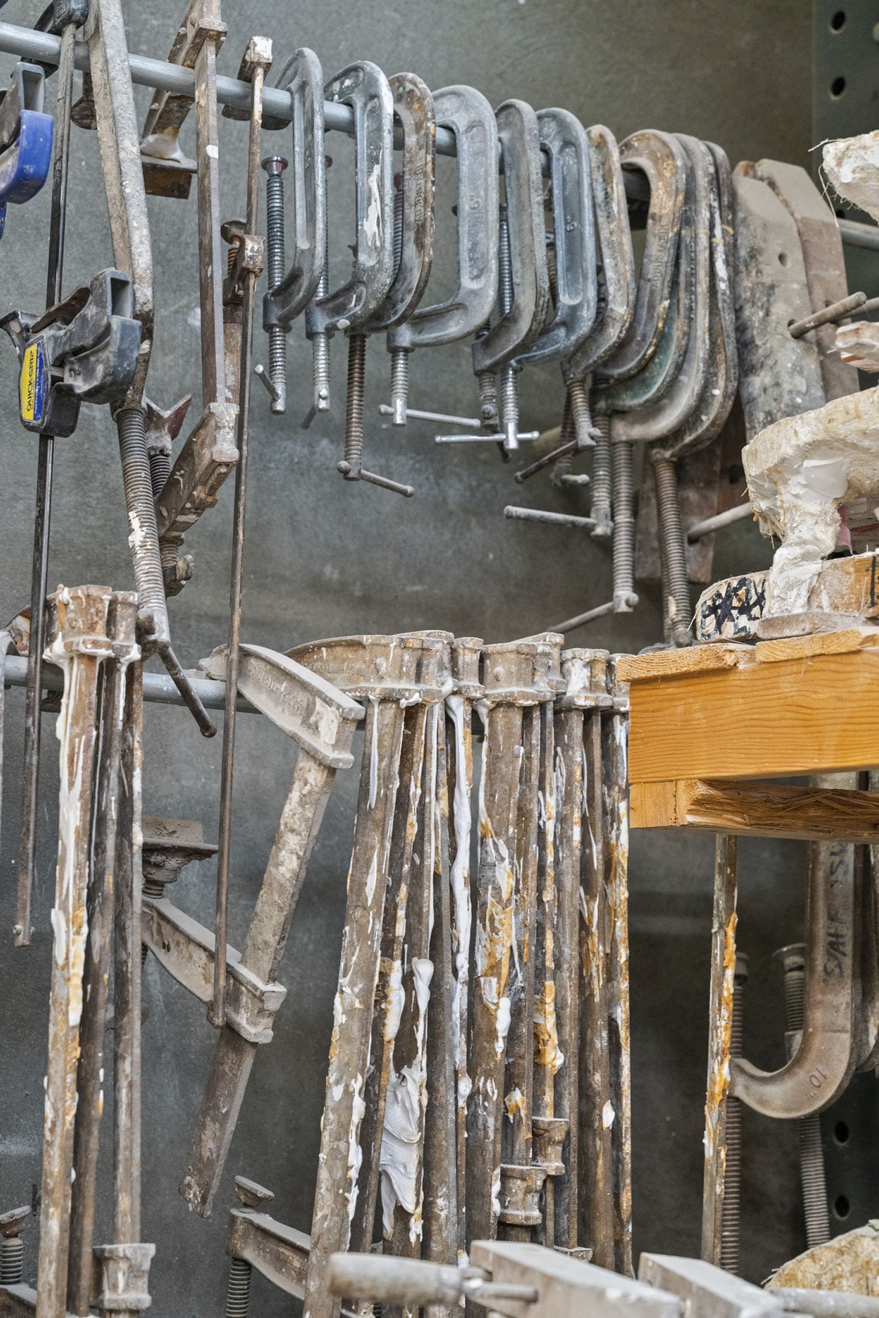 A wall of used C-clamps and plaster-coated molds in a workshop.