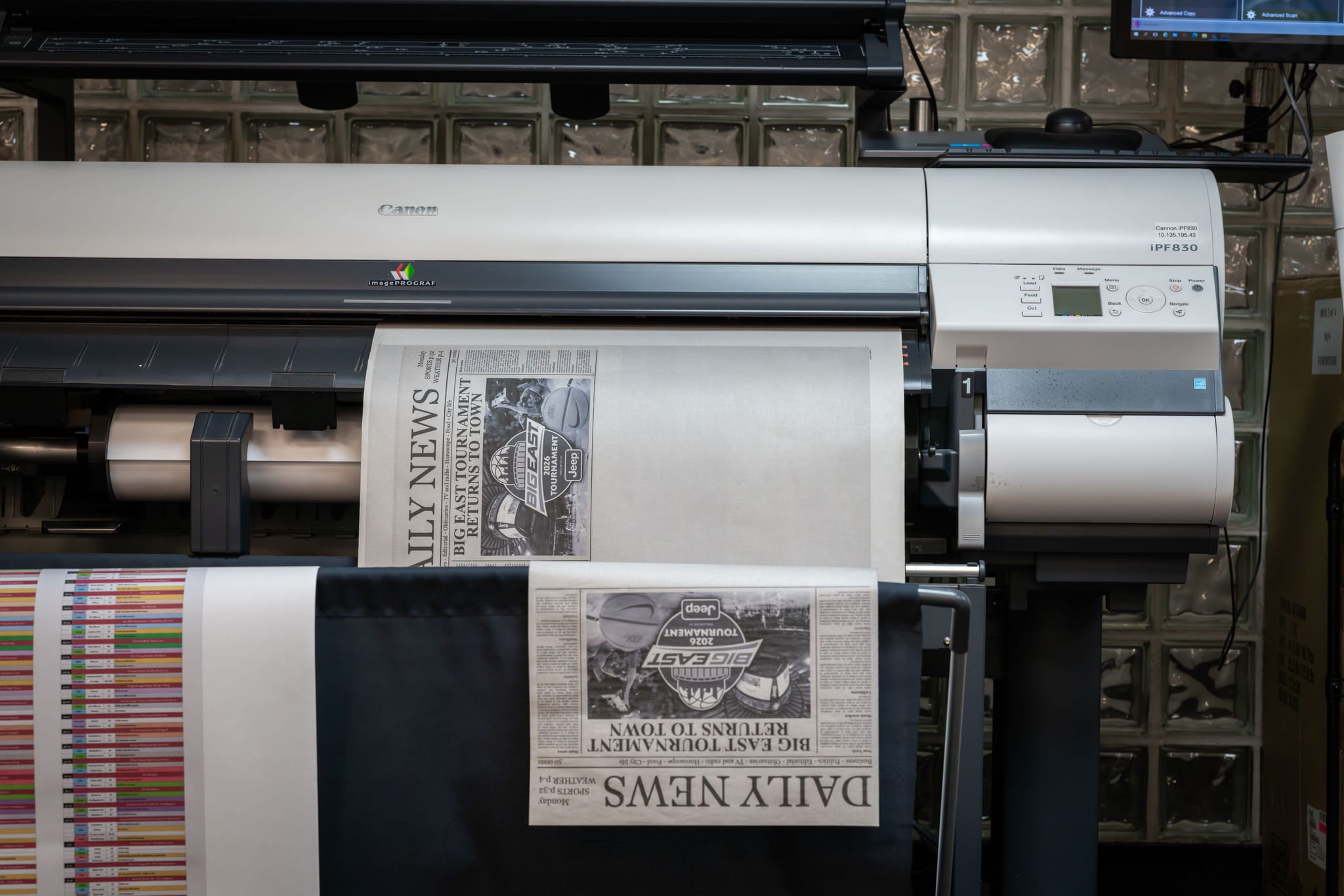 A Canon iPF830 large format printer outputting a newspaper-style graphic on a roll of paper.