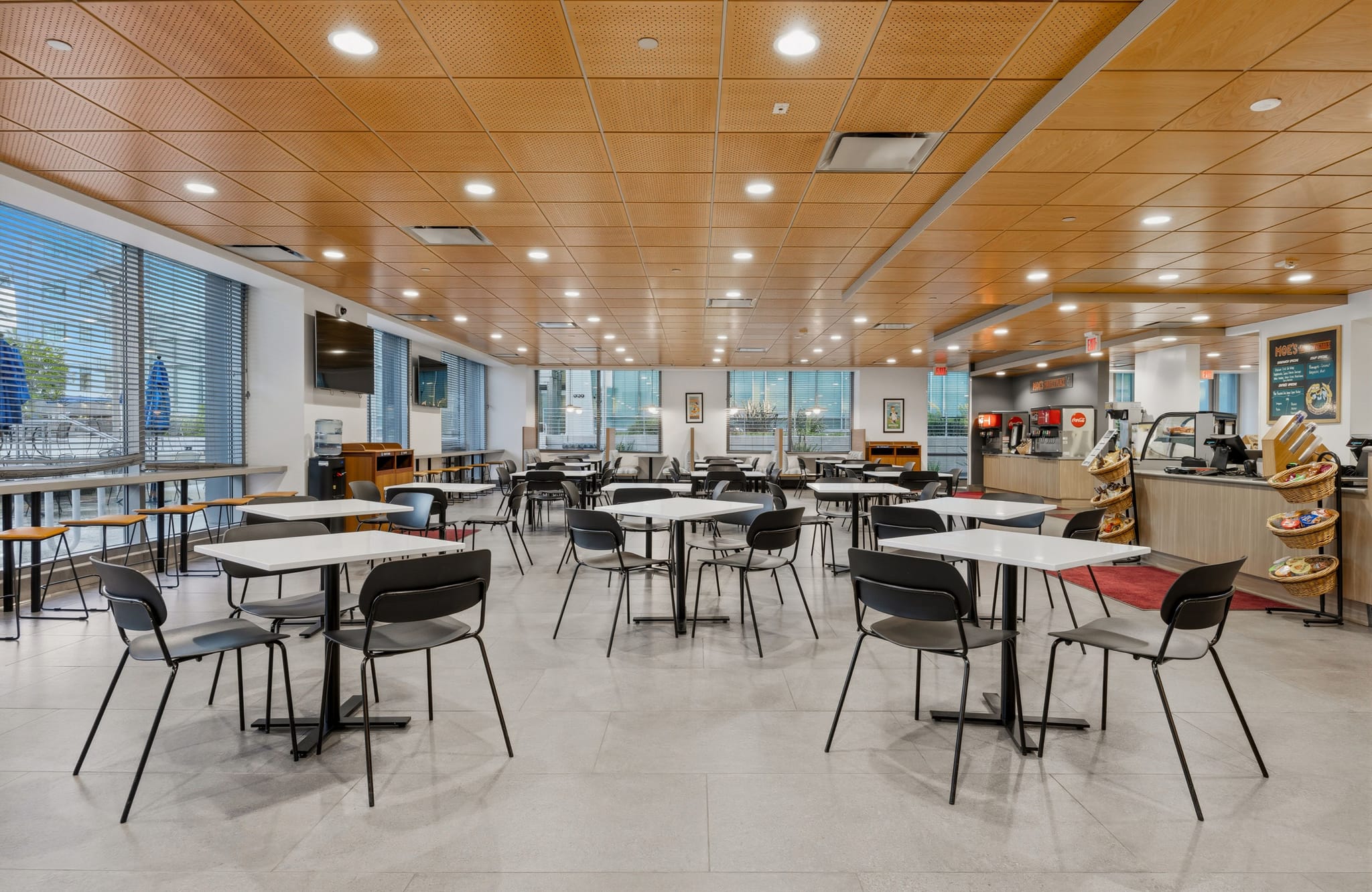 Empty modern cafeteria with white tables, black chairs, and a service counter.