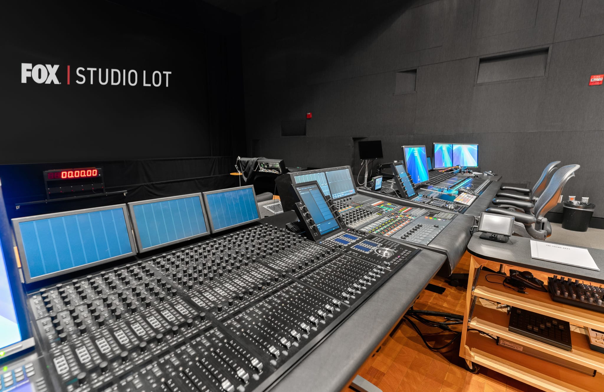 A control room featuring a large audio mixing console, multiple screens, and a "FOX | STUDIO LOT" logo on the wall.
