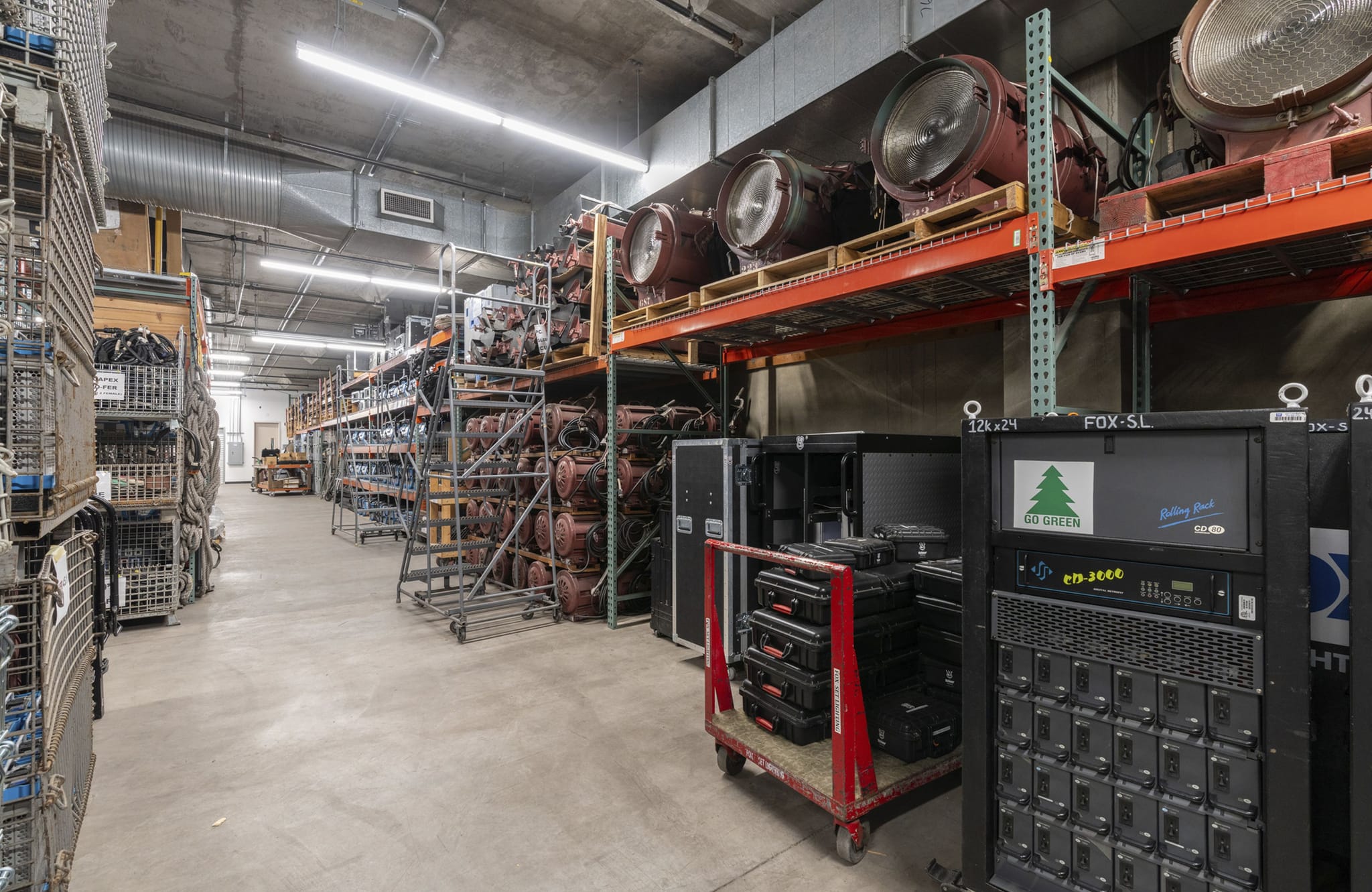 Industrial warehouse with rows of shelves displaying large stage lights and production equipment.