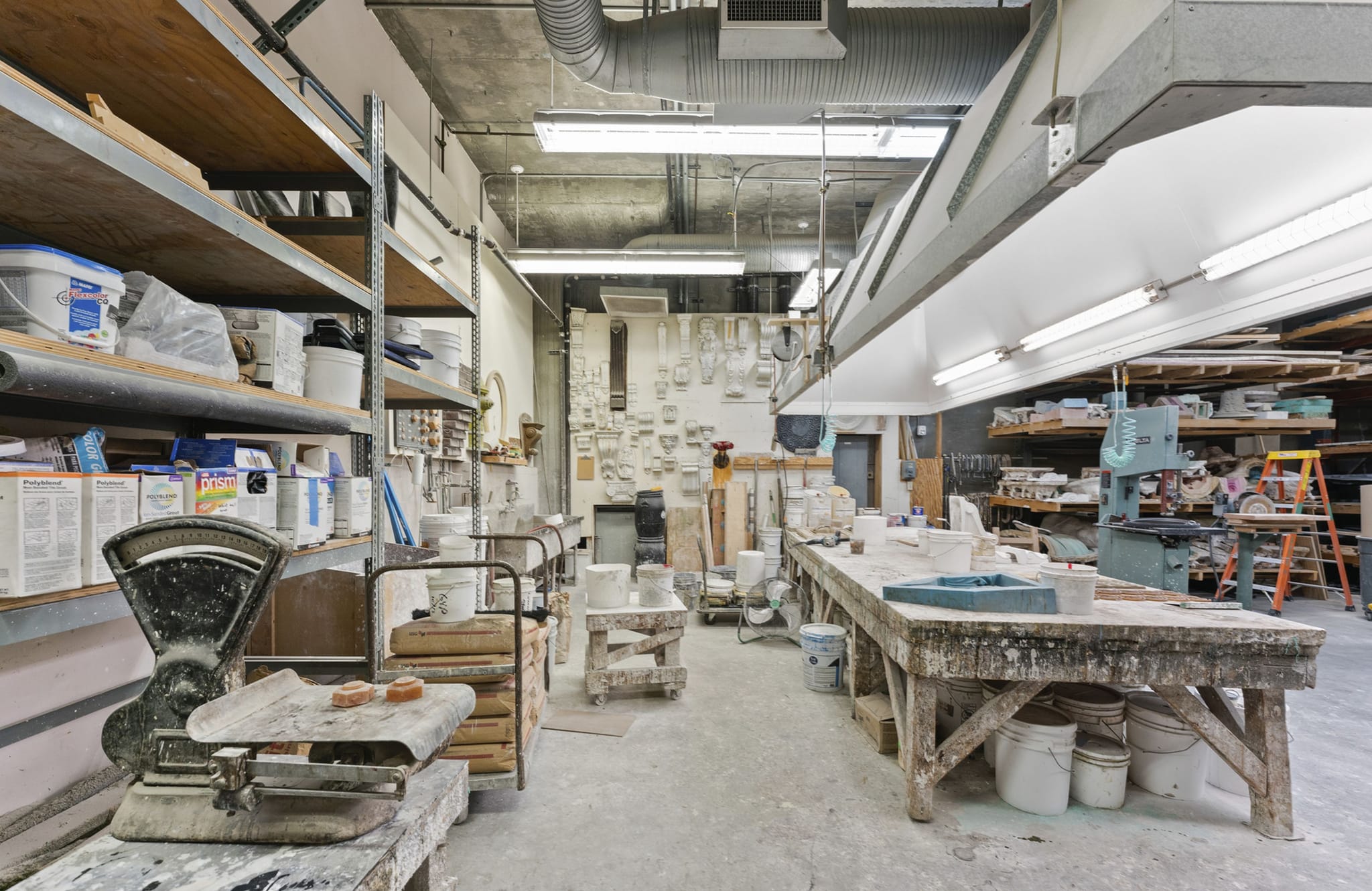 A busy ceramics or casting workshop with shelves of materials, a large worktable, and various tools.