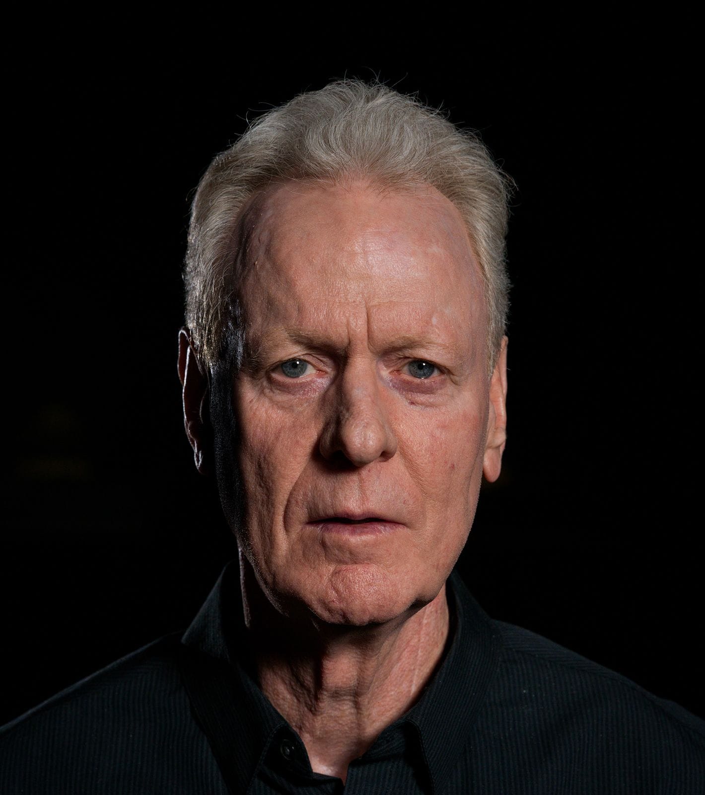 Headshot of an older man with grey hair and a serious expression against a dark background.