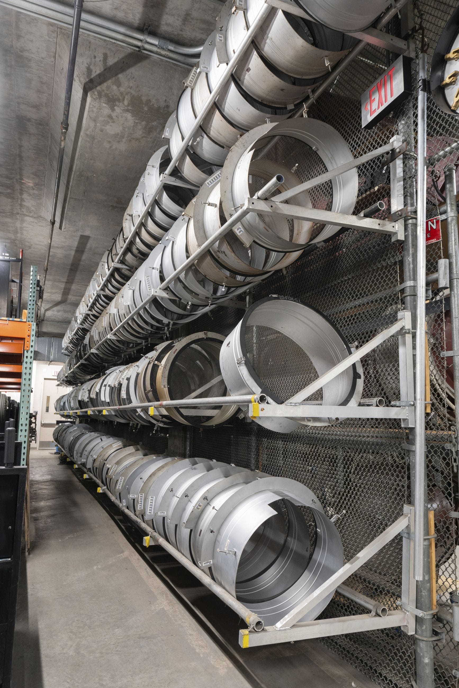 Three rows of circular metal lighting components on shelves in a warehouse.