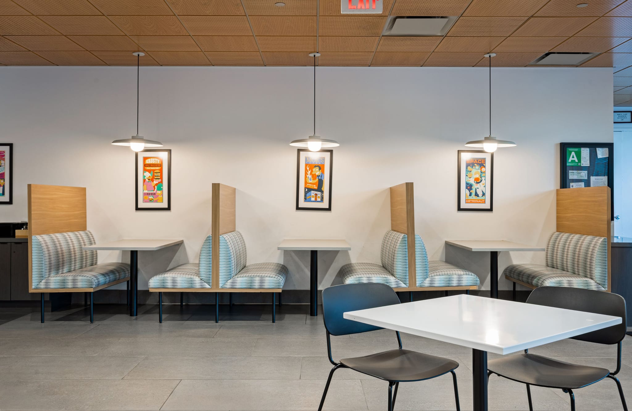 A bright dining room with several striped booths and white tables, accented by colorful wall art and pendant lights.