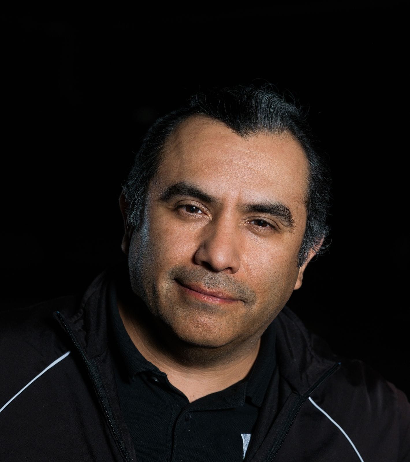 Portrait of a man with dark, greying hair and a subtle smile, wearing a black jacket.