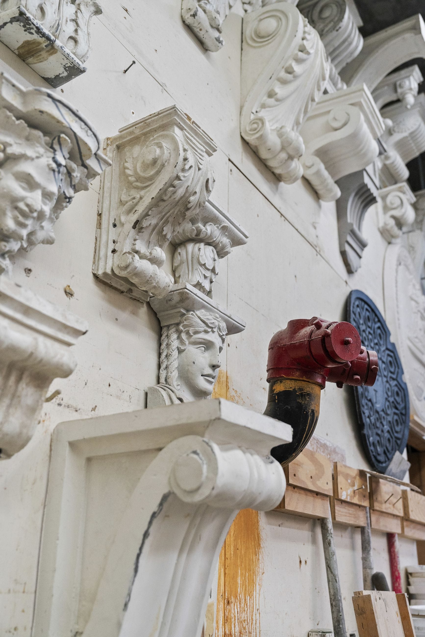 Ornate white architectural elements including corbels and busts mounted on a light wall, next to a red fire hydrant connection.