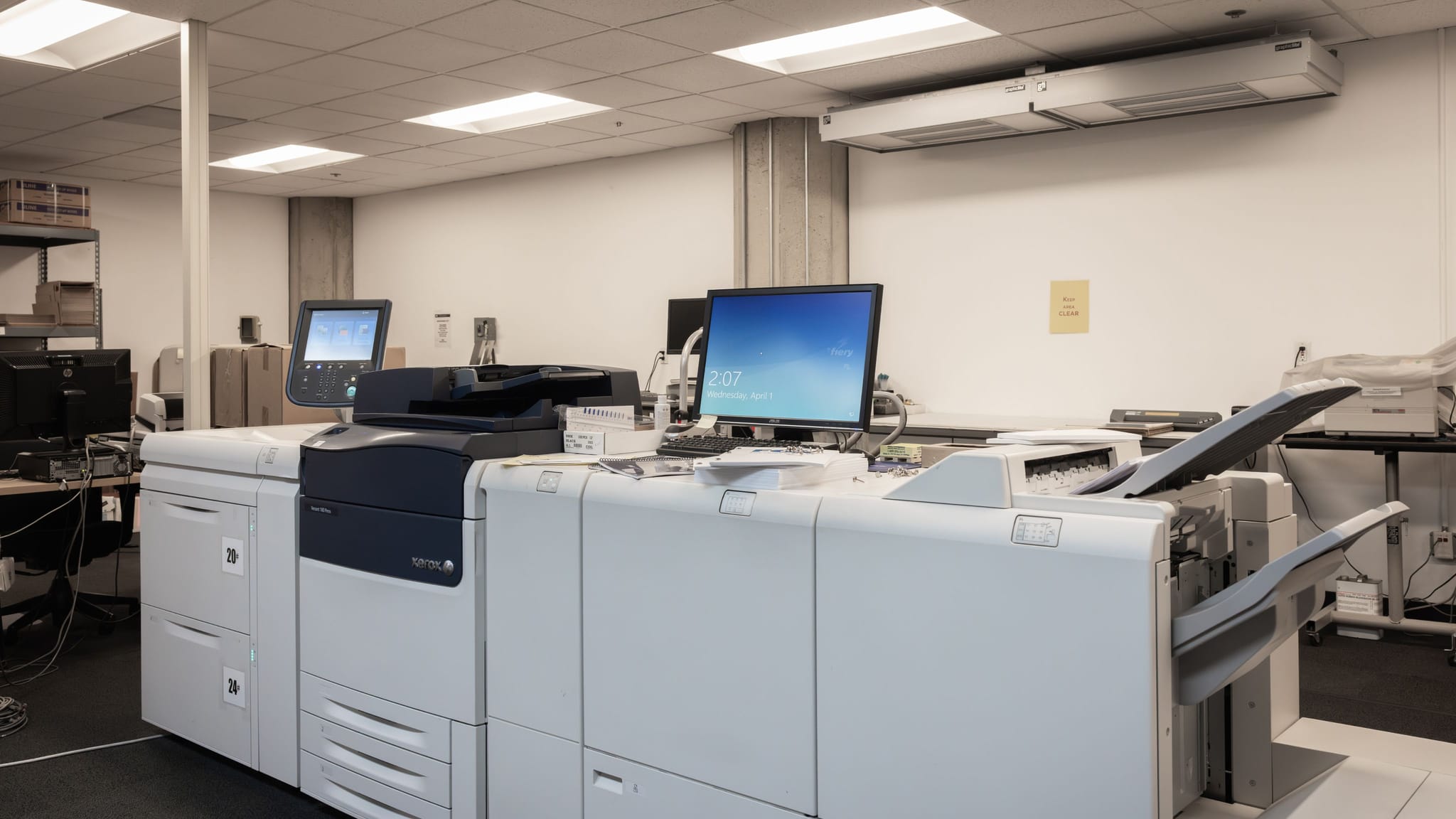 Large professional printing equipment and computer monitors in a bright office.