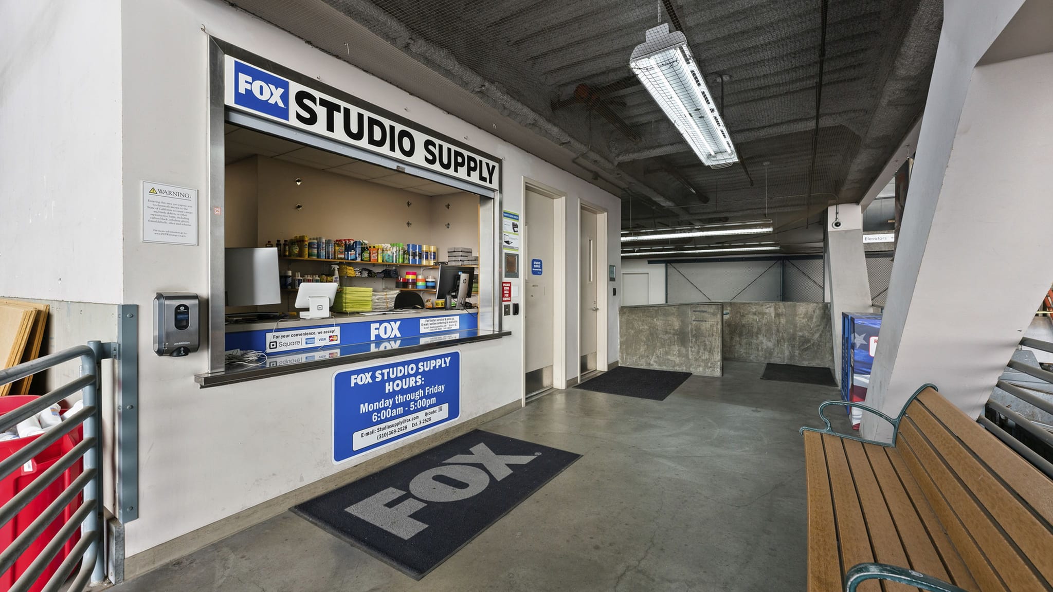 A Fox Studio Supply counter with products, a Fox logo mat, and a wooden bench in an industrial-style hallway.