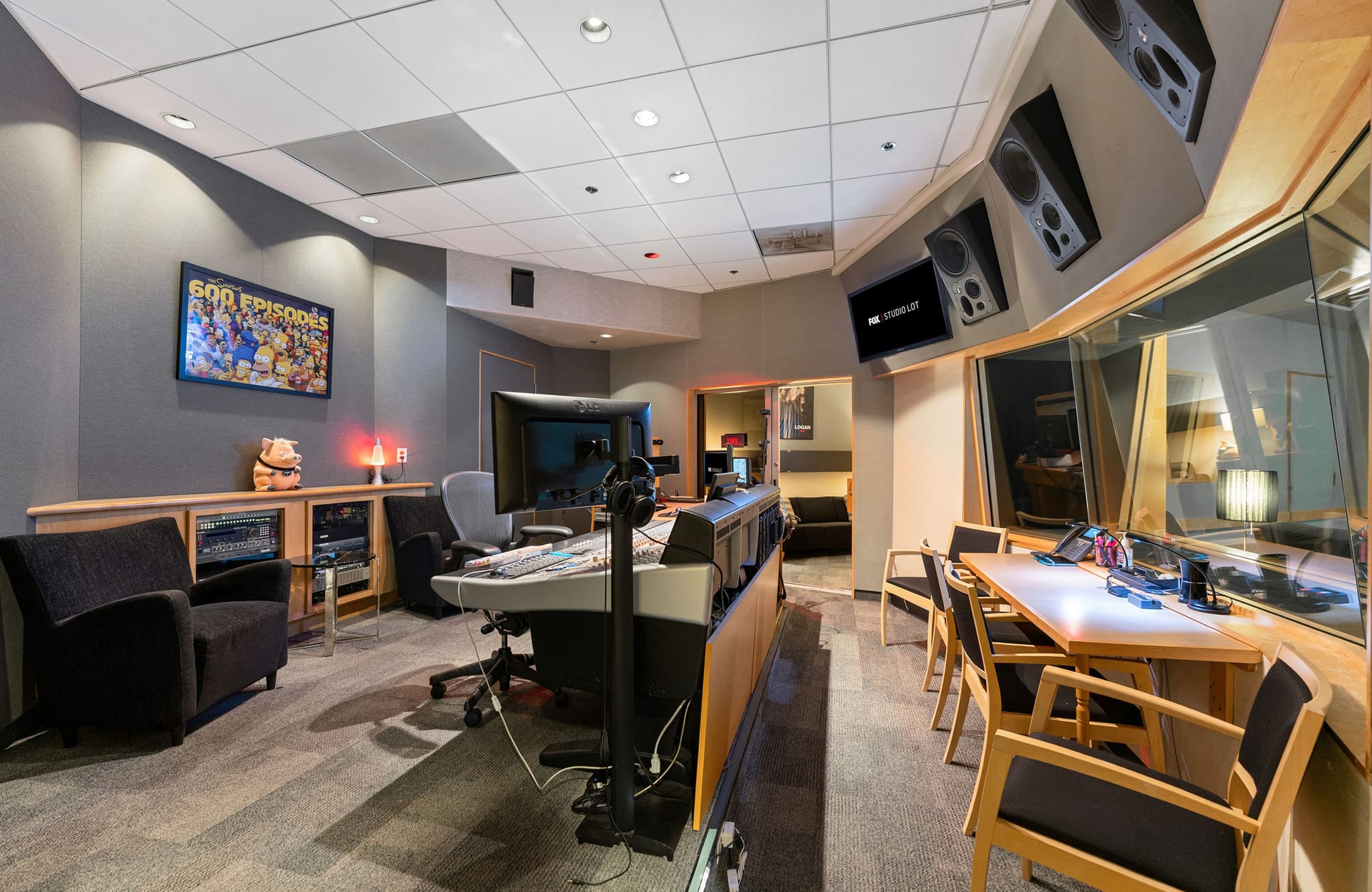 A professional audio recording studio control room with a mixing console and a large window looking into a soundproofed booth.