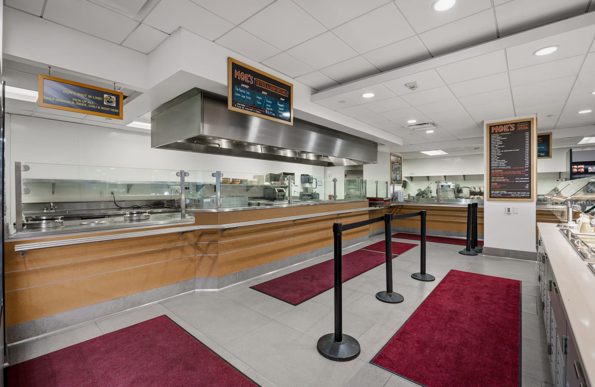 Empty cafeteria serving line with a Moe's Southwest Grill menu, stainless steel counters, and red queue mats.
