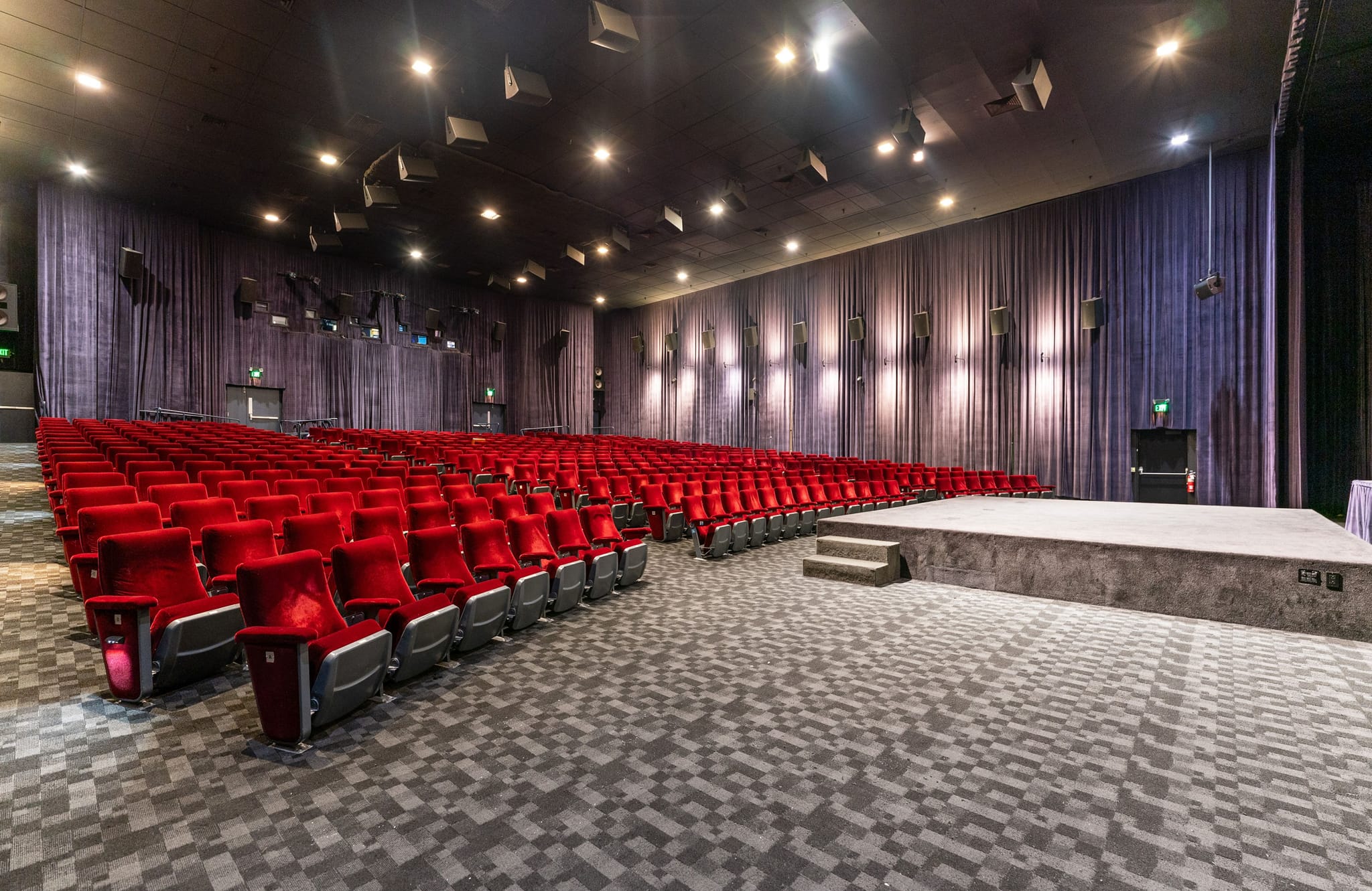Empty modern auditorium with rows of red seats, a stage, and purple curtains.
