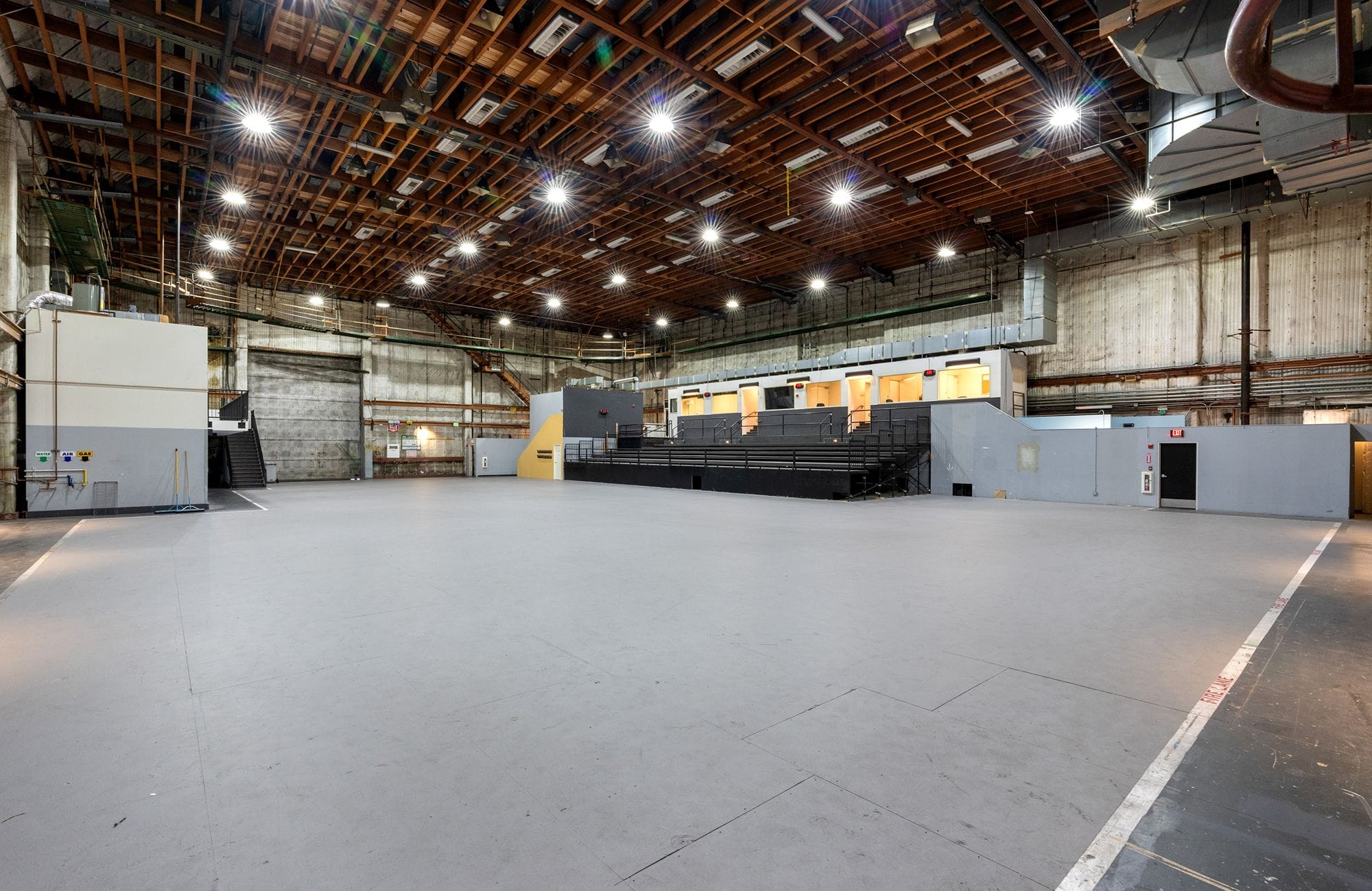 Large, empty studio with high exposed wooden beam ceiling, bright lights, and tiered seating.