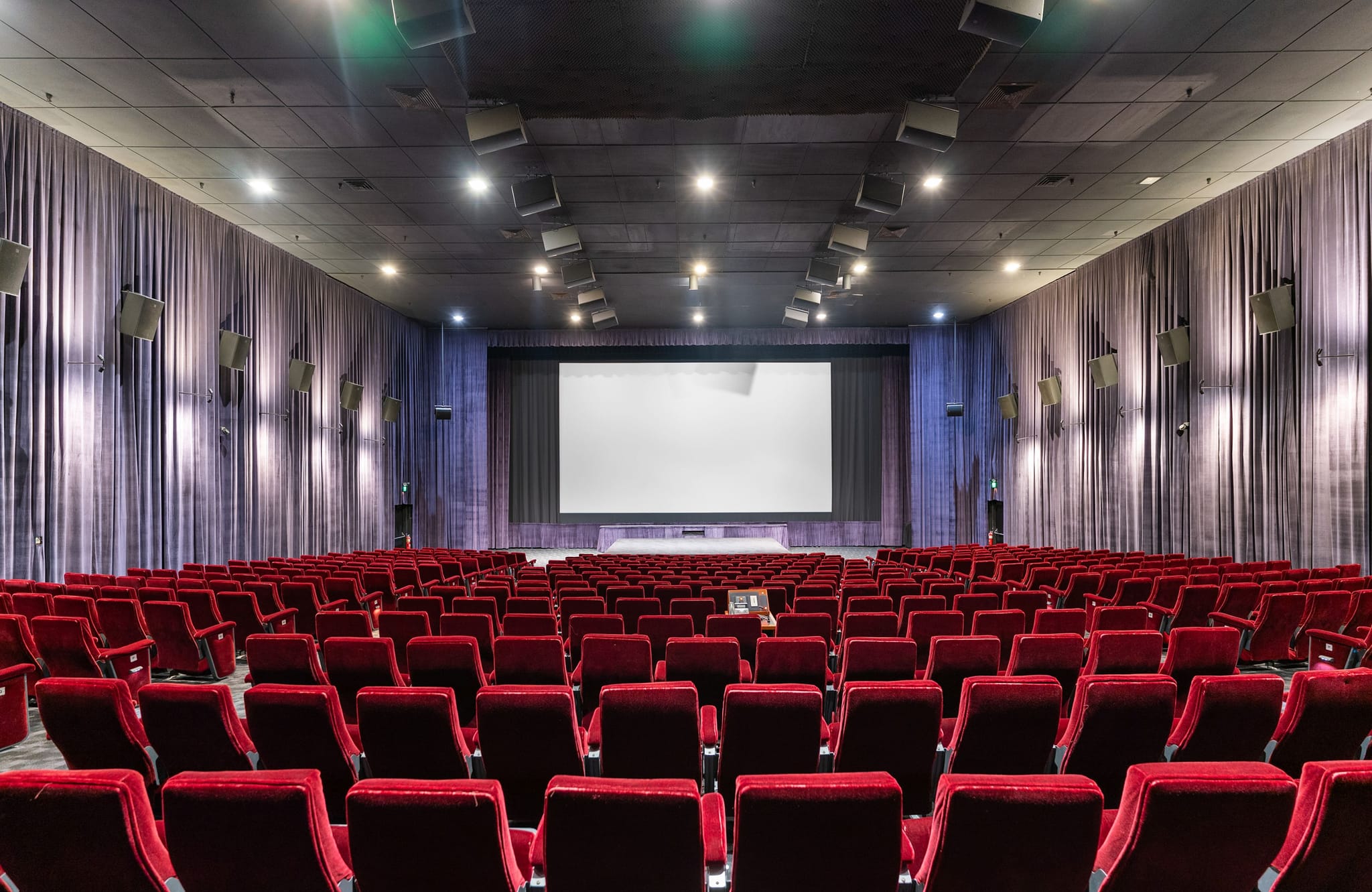 Empty movie theater with rows of red seats and a large blank screen.