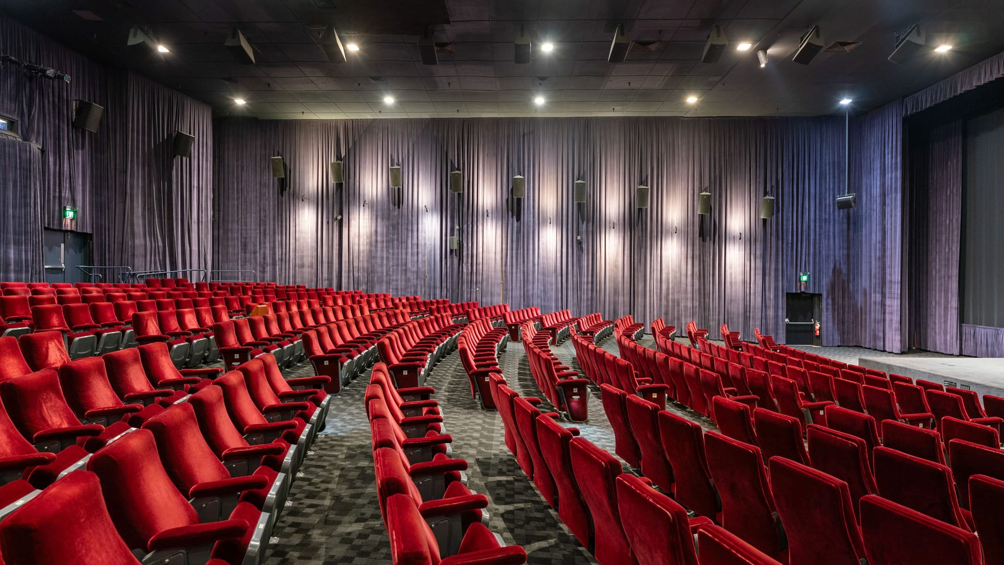 Empty cinema with rows of red velvet seats and a screen.