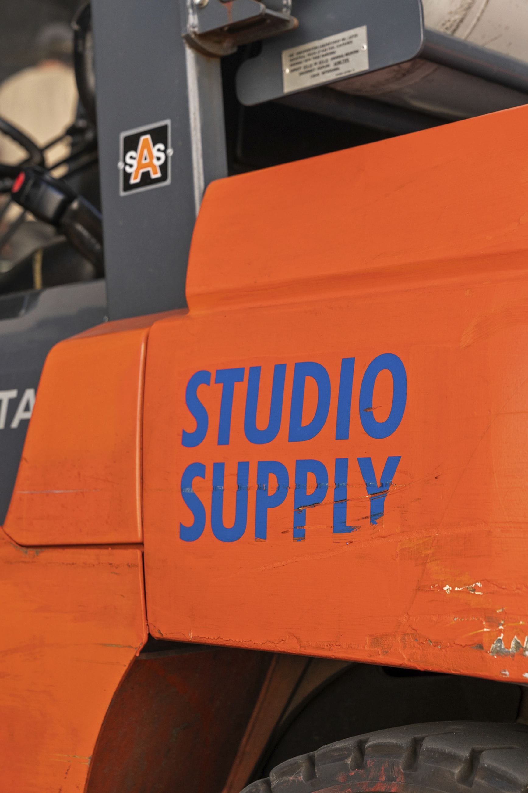 Orange forklift with "STUDIO SUPPLY" in blue text on its side.