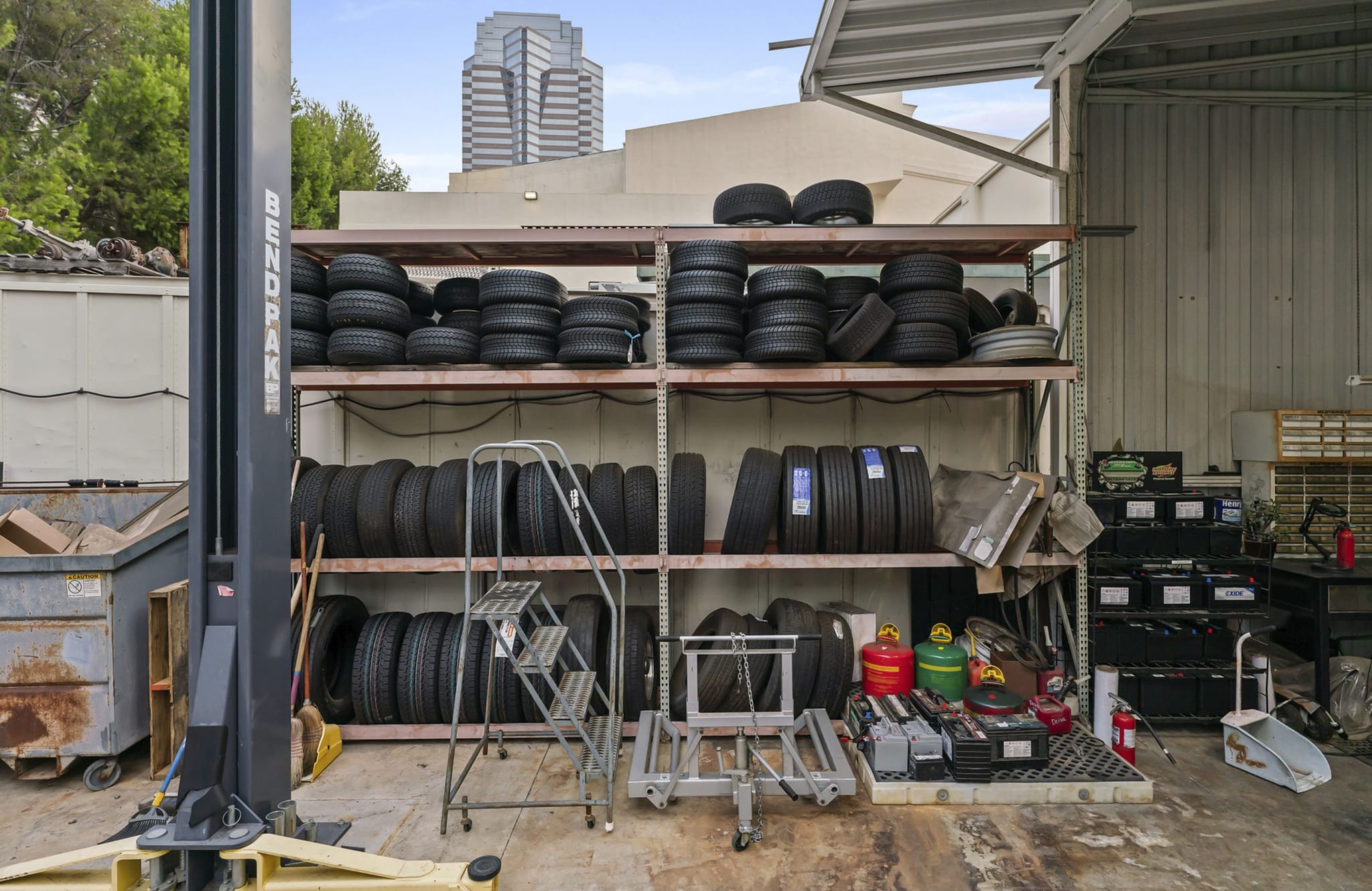 An auto shop bay with a car lift, metal shelves full of tires, and various equipment.