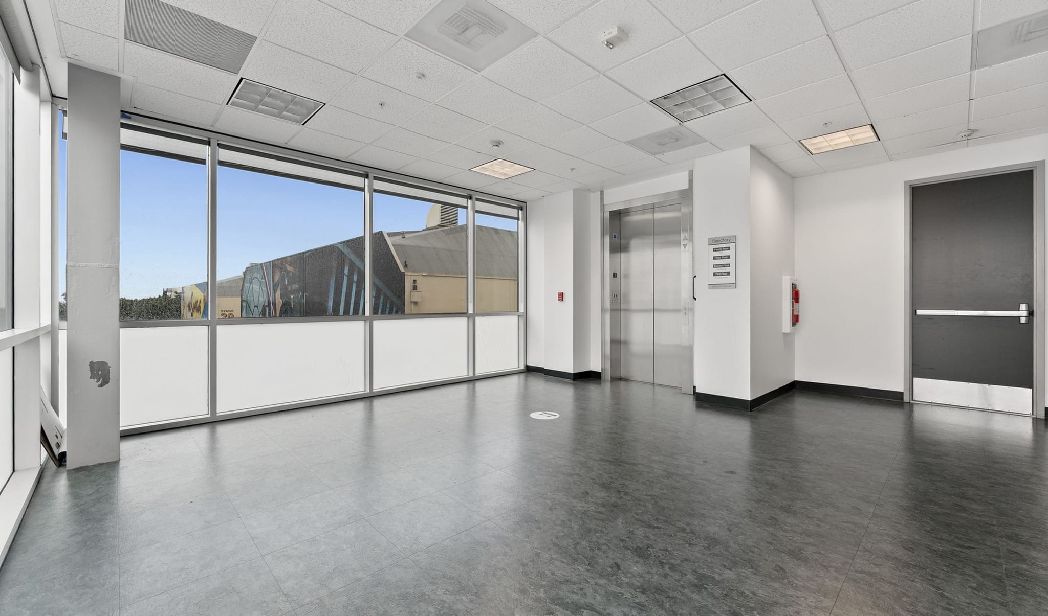 Empty modern commercial space with large windows, an elevator, and a dark floor.