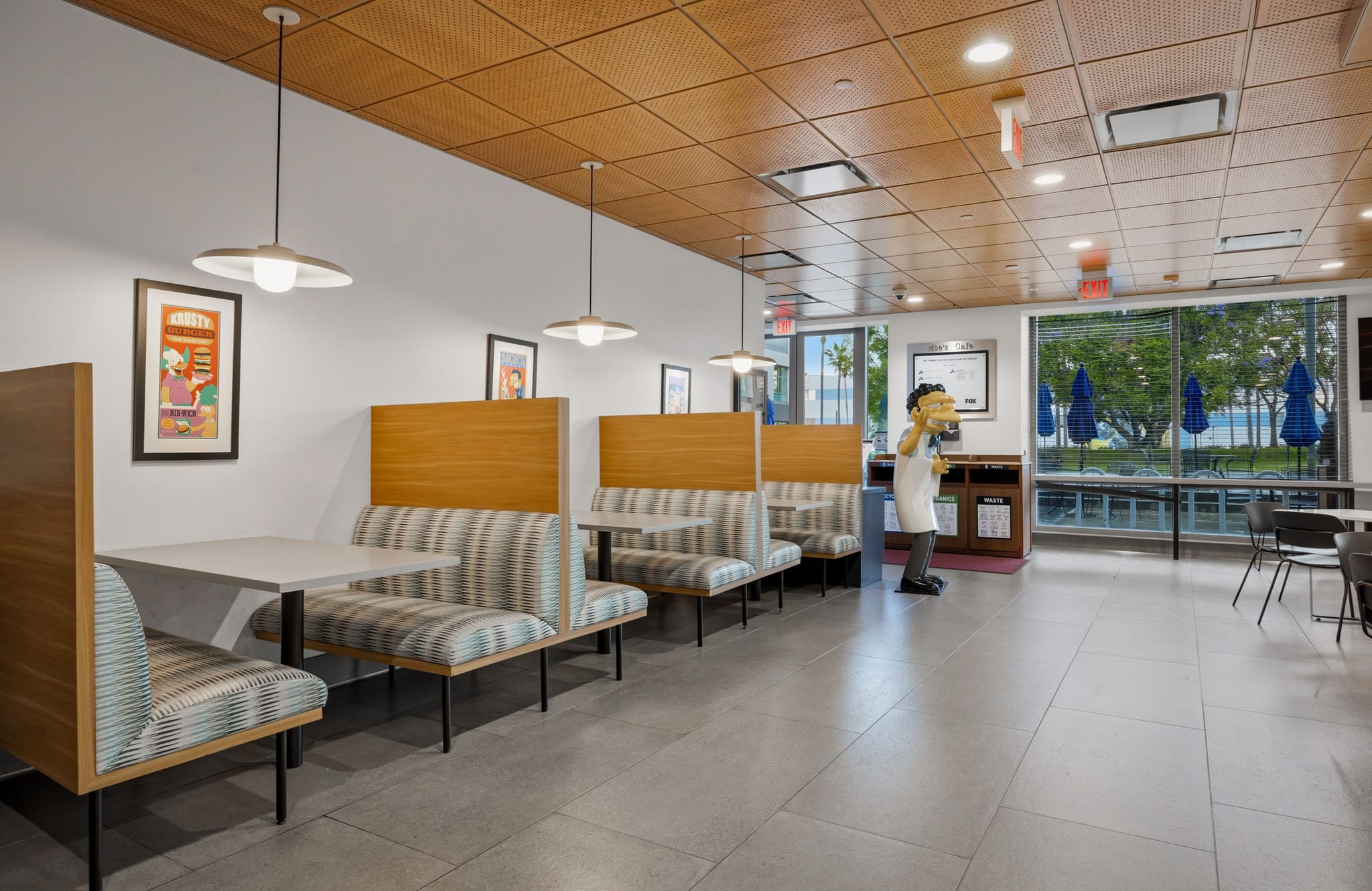 A modern diner with striped booth seating, pendant lights, a chef statue, and a window view of an outdoor patio with blue umbrellas.