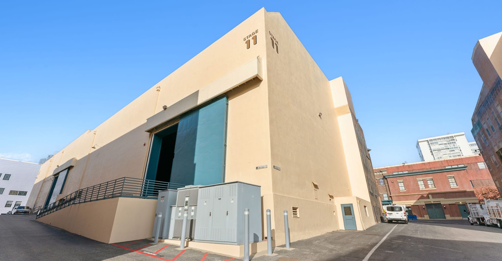 A large tan building labeled "STAGE 11" with a blue loading door, viewed from an alleyway.