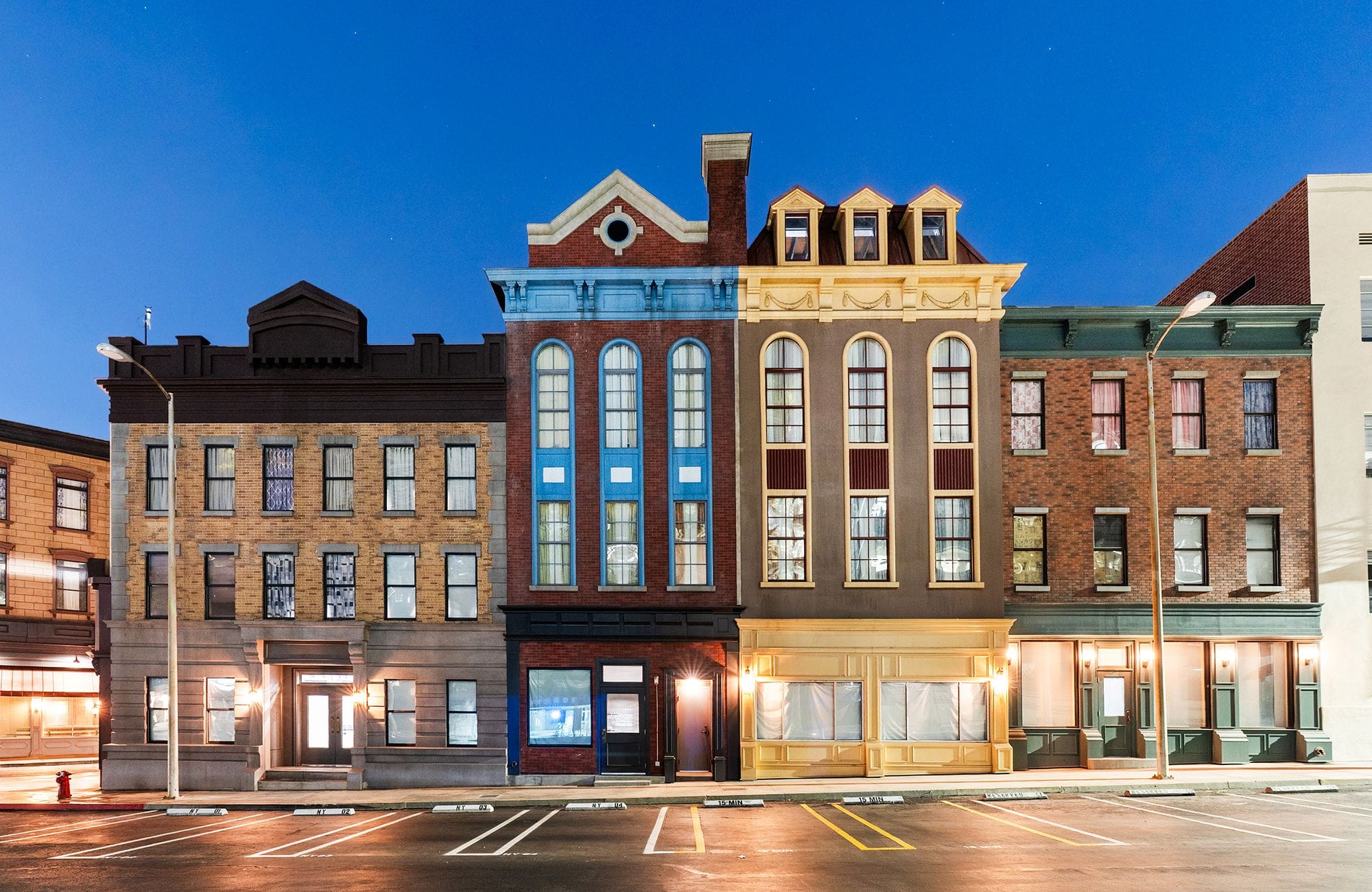 A row of diverse-style buildings lines a street with parking spaces at night.